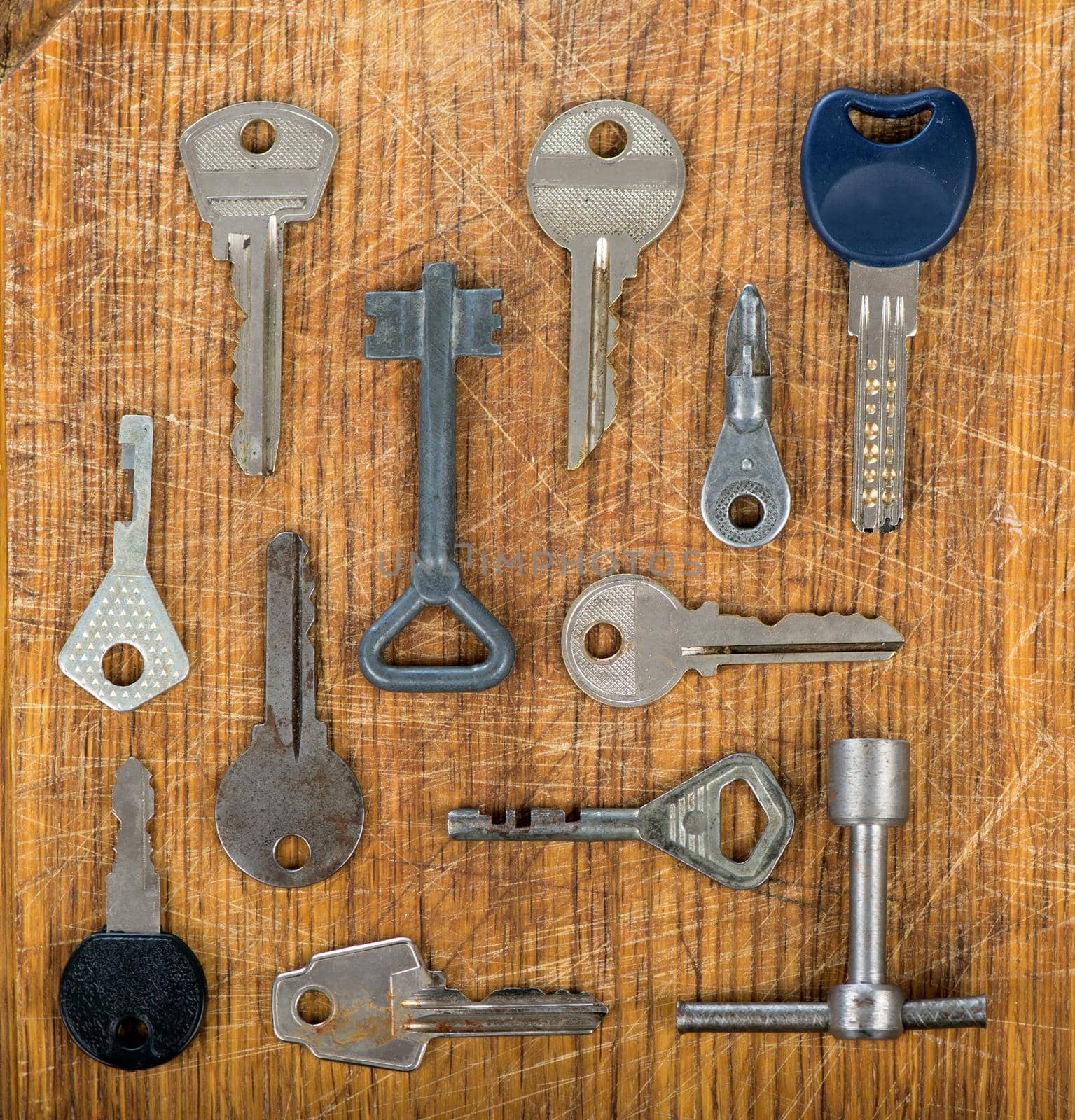 Many assorted old multi-colored metal antique vintage keys of different shapes on wooden scratched table background. by aprilphoto