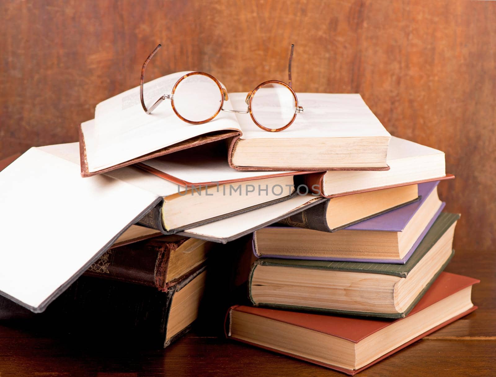 Old hardcover books and vintage glasses with round lenses against a dark background by aprilphoto