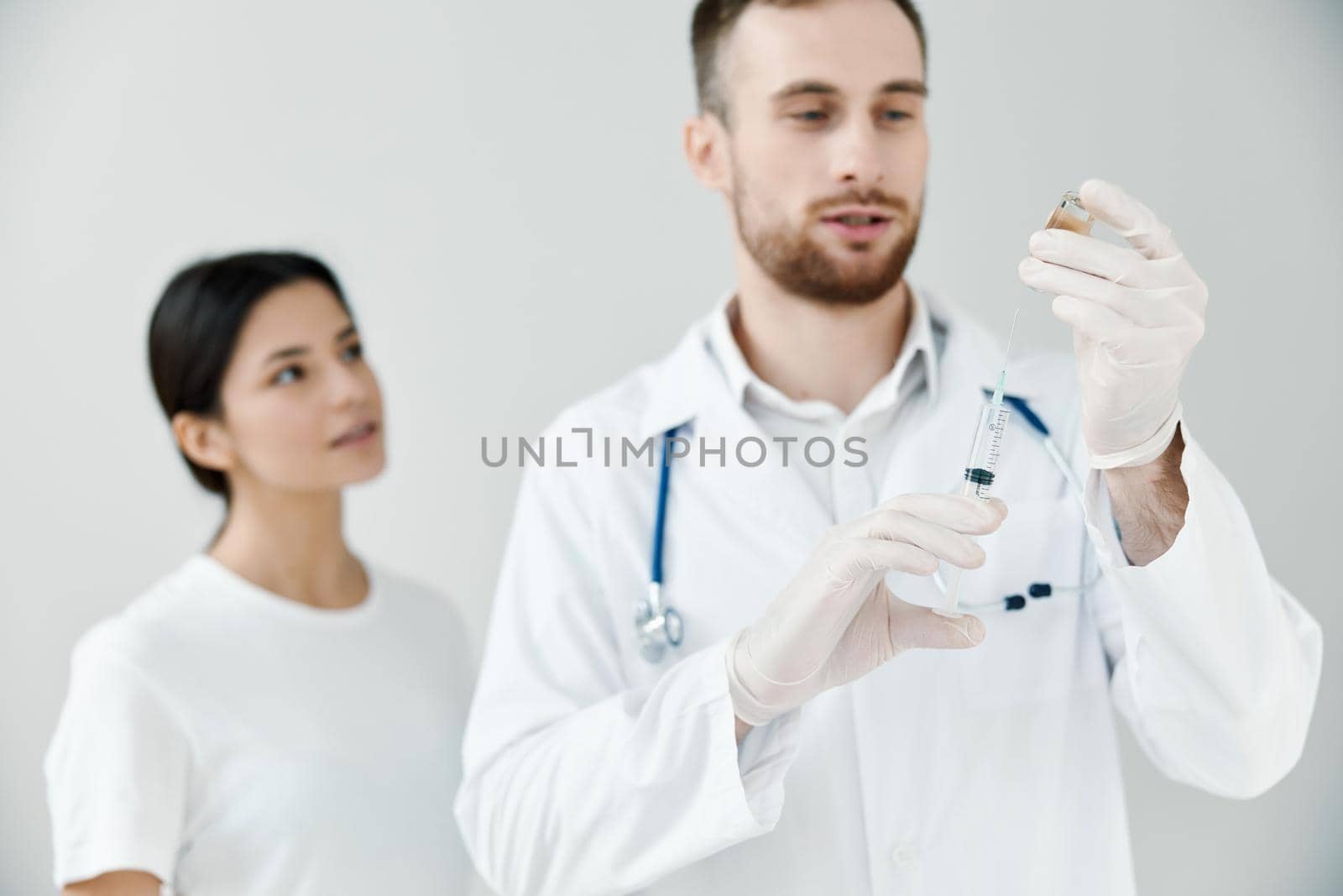 covid-19 vaccination doctor with otoscope and syringe patient in the background by SHOTPRIME