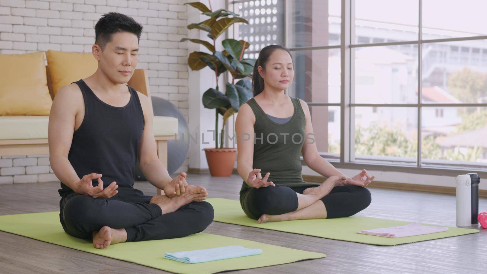 Happy Asian beautiful lifestyle family couple doing YOGA sitting meditating on lotus pose workout at home together on mat with eyes closed. Two people sport healthy concept.