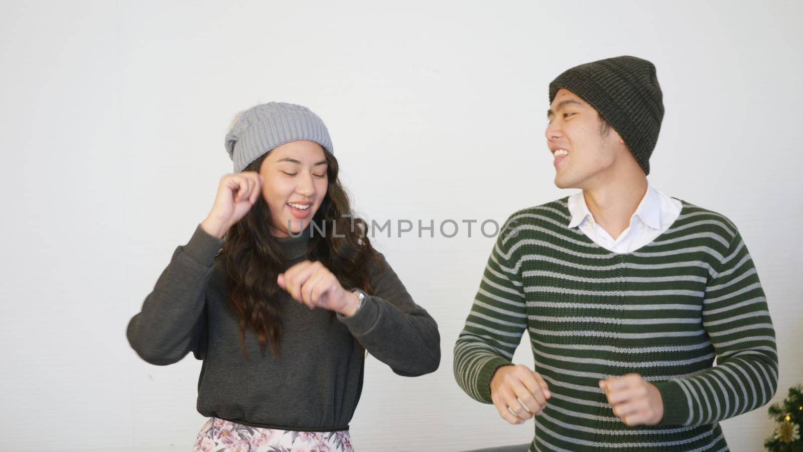 Happy Asian beautiful young family couple lifestyle husband and wife smile dancing laughing around christmas tree at home living room, man and woman are enjoying spending time together,