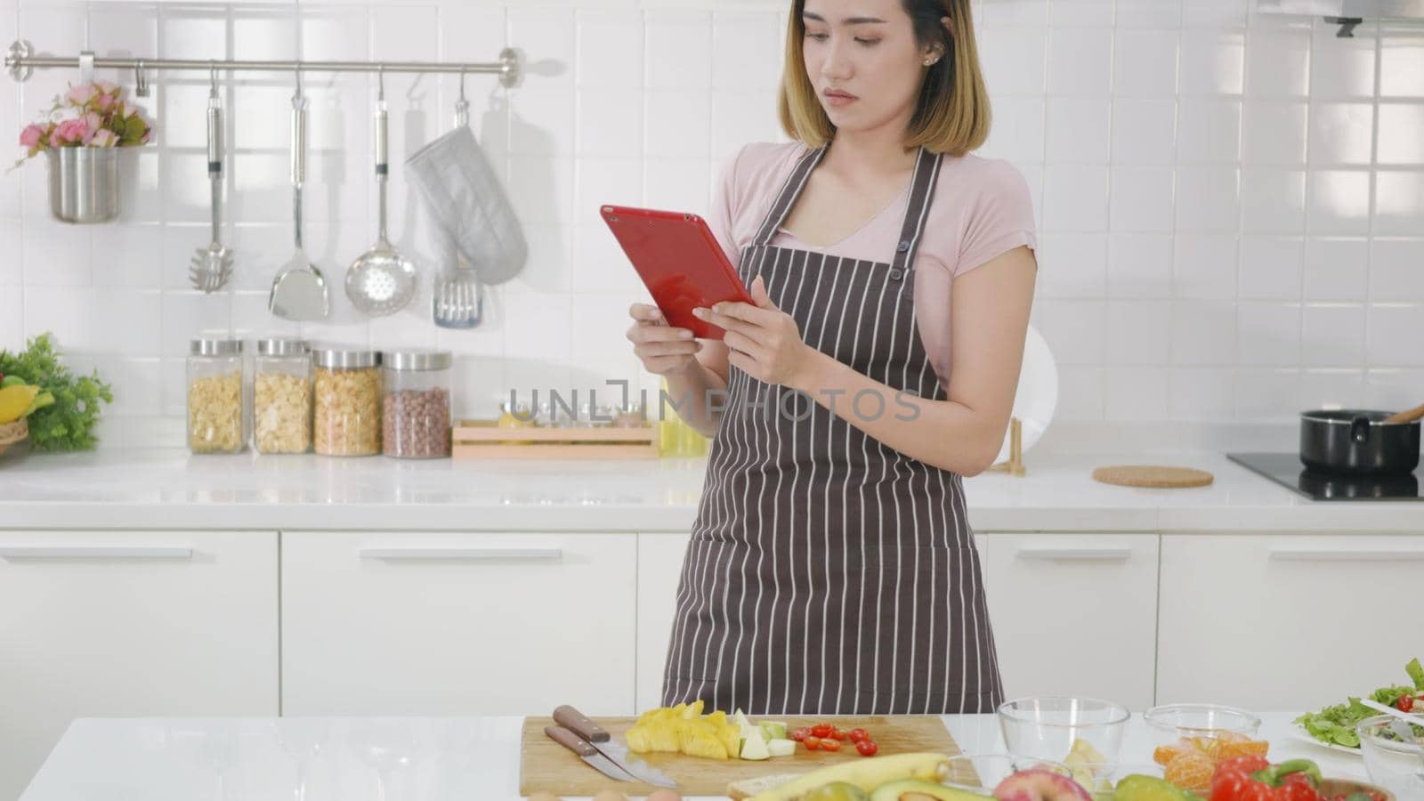 woman in kitchen following recipe on digital tablet computer by Sorapop