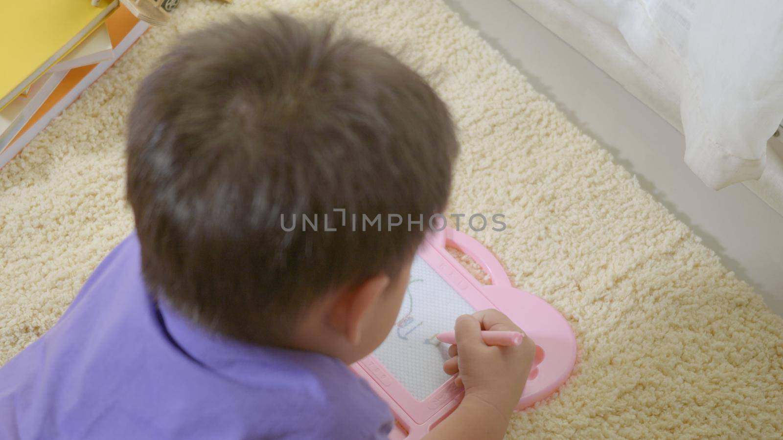 Happy Asian klid little boy preschool writing at the magnetic drawing board at home on carpet. Funny child playing magnetic drawing board. Education Learning to draw concept. Back view