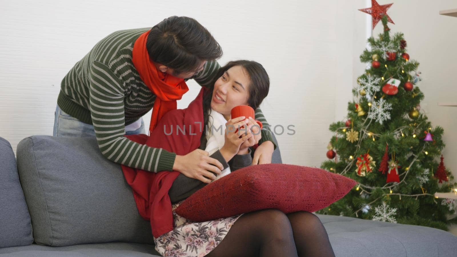 Happy Asian beautiful young family couple husband and wife on sofa in home living room, Loving man covering blanket to woman sit on sofa drink tea showing care warming, winter holidays concept