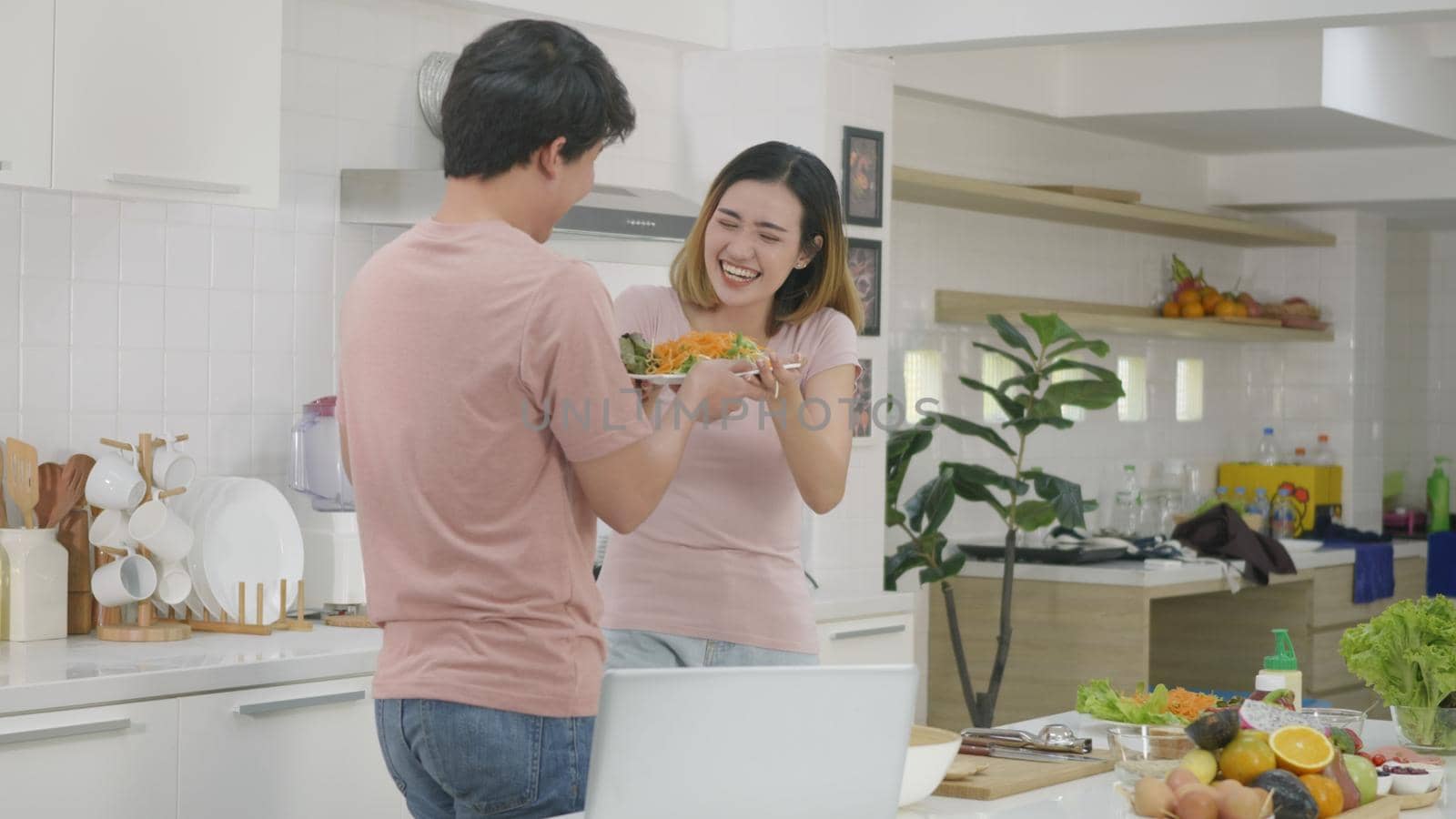 Happy Asian beautiful family couple husband and wife cooking vegetable salad in kitchen together at home. The man kiss woman for thank you. healthy food concept