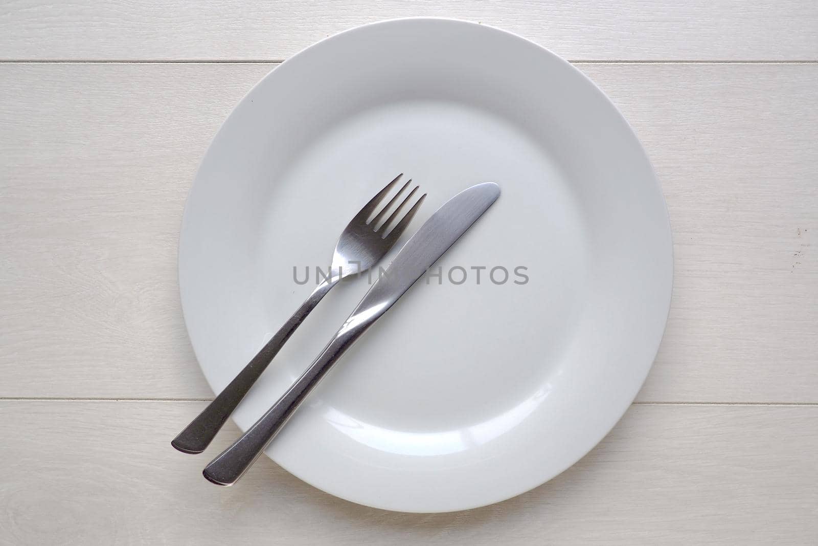 White plate and knife and fork on white wooden background by fivepointsix