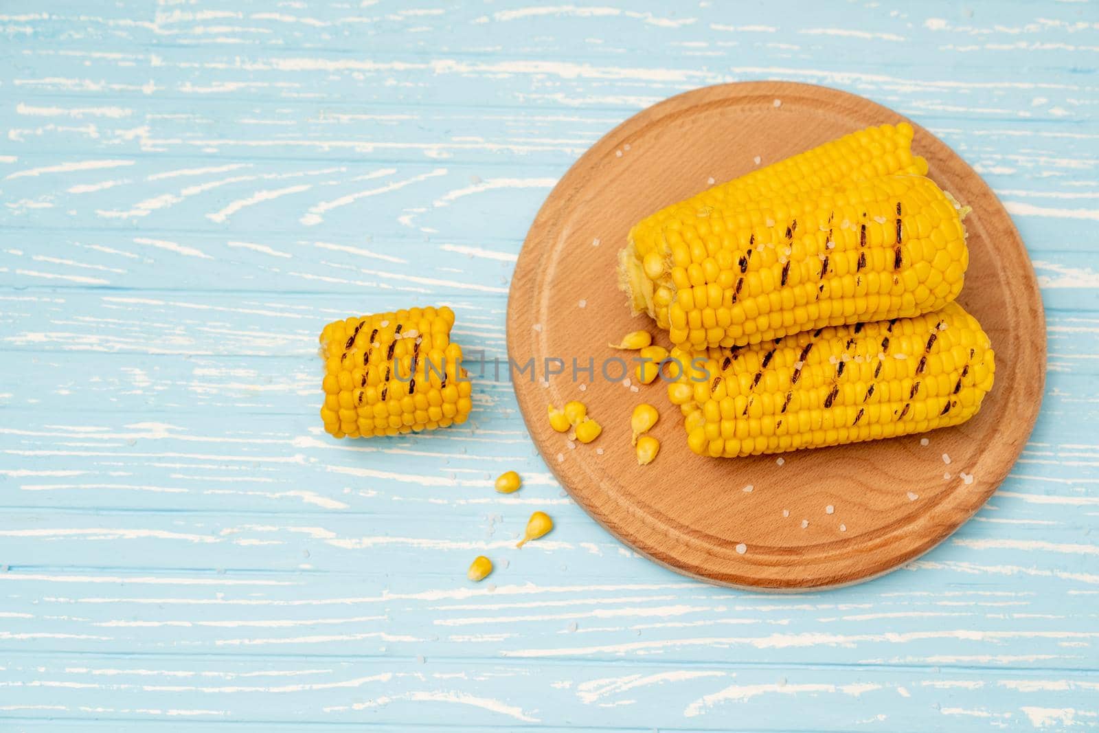 Grilled hot Corn cob lies on round cutting board plate blue wooden table background. Copy space for text.