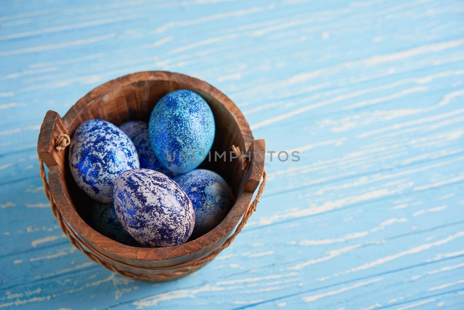 Blue chicken eggs lie in round wooden basket which stands on a blue wooden table. Easter background. Seasonal holiday flat lay with free space for text. Classic blue color of the year 2020