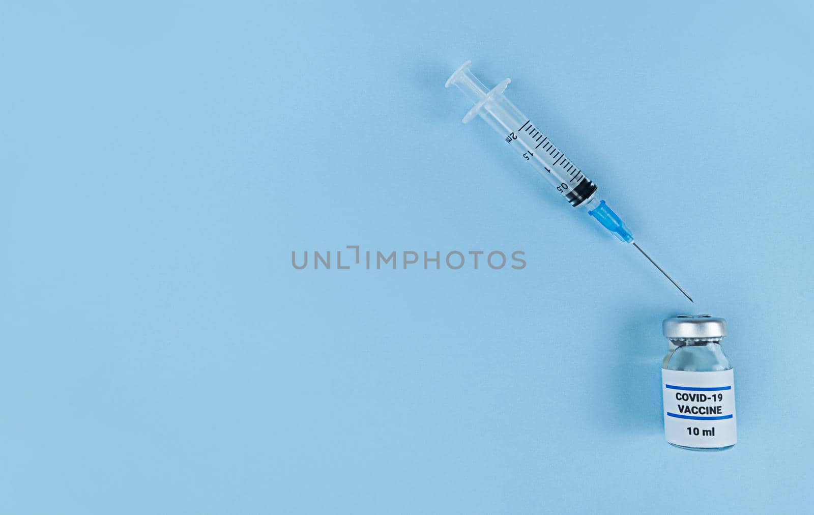 Single use syringe and medical bottle with coronavirus vaccine on a blue background with copy space.