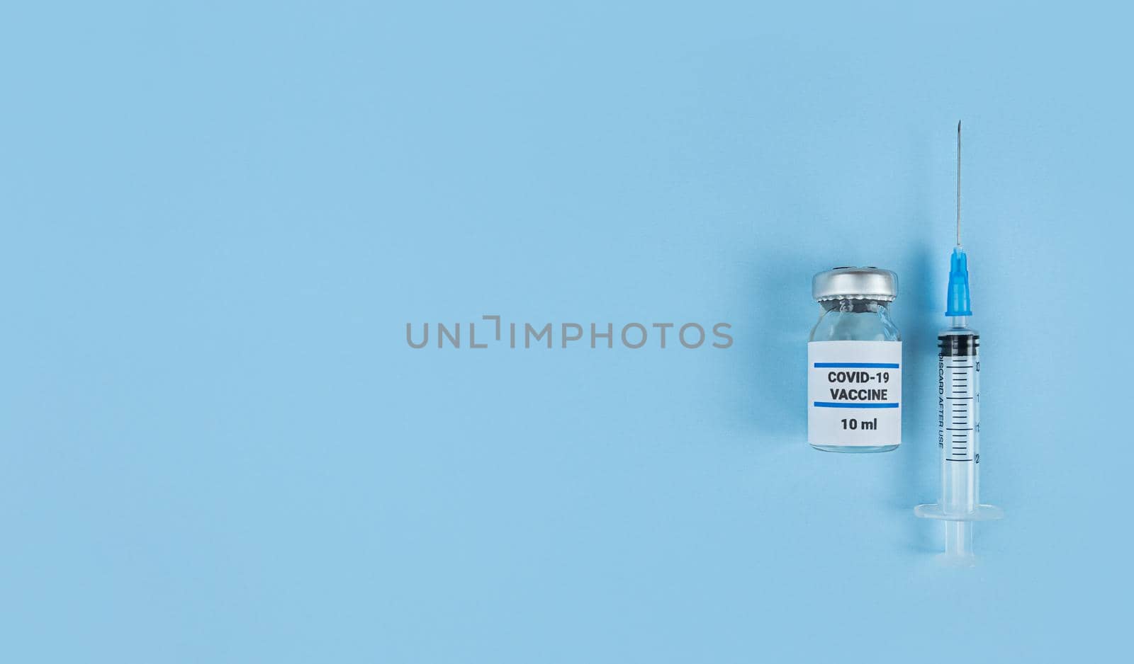 Single use syringe and medical bottle with coronavirus vaccine on a blue background with copy space.
