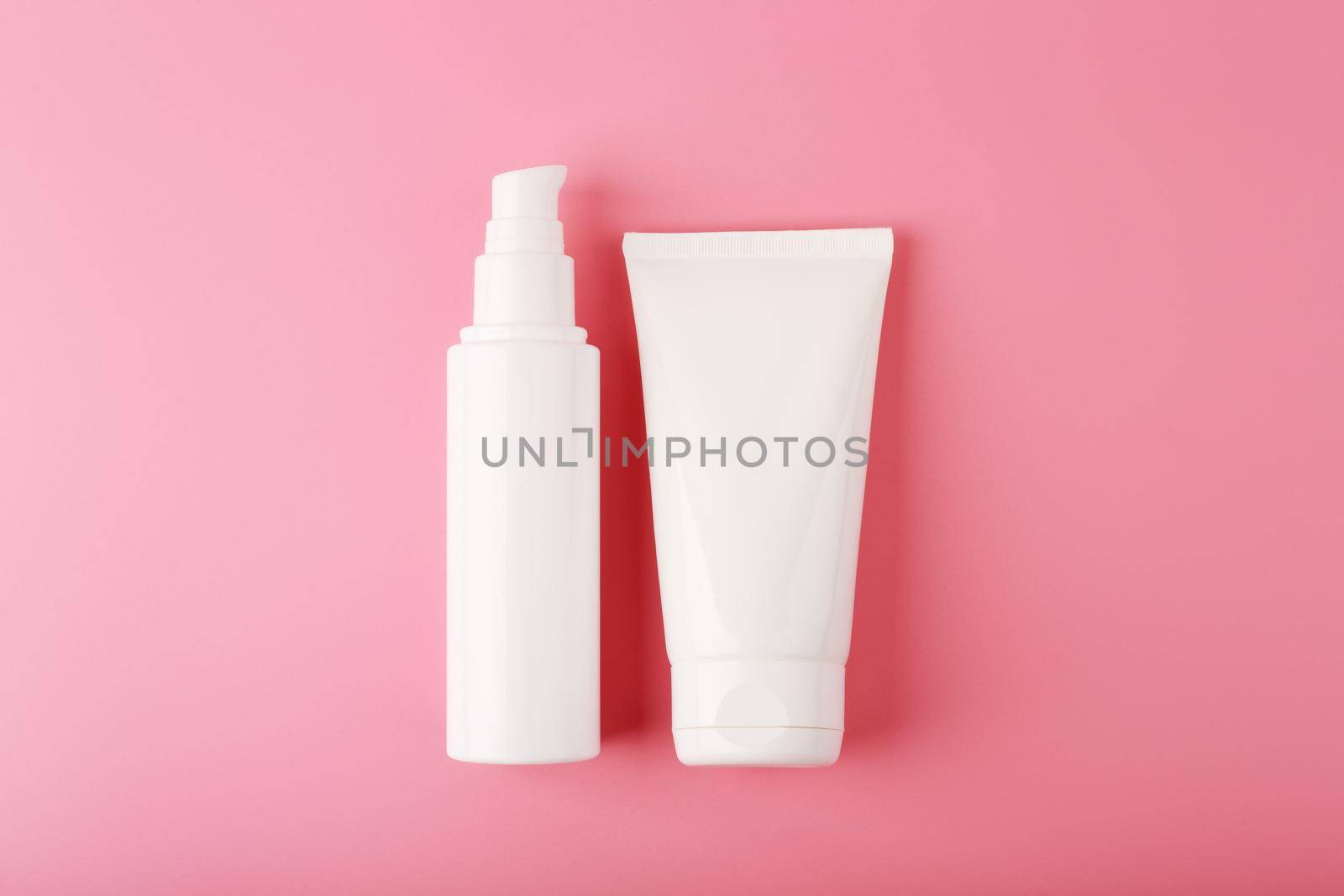 Minimalistic flat lay with two white cream tubes on pink background. Concept of beauty products for skin hydration, moisturizing, anti aging treatment of exfoliation