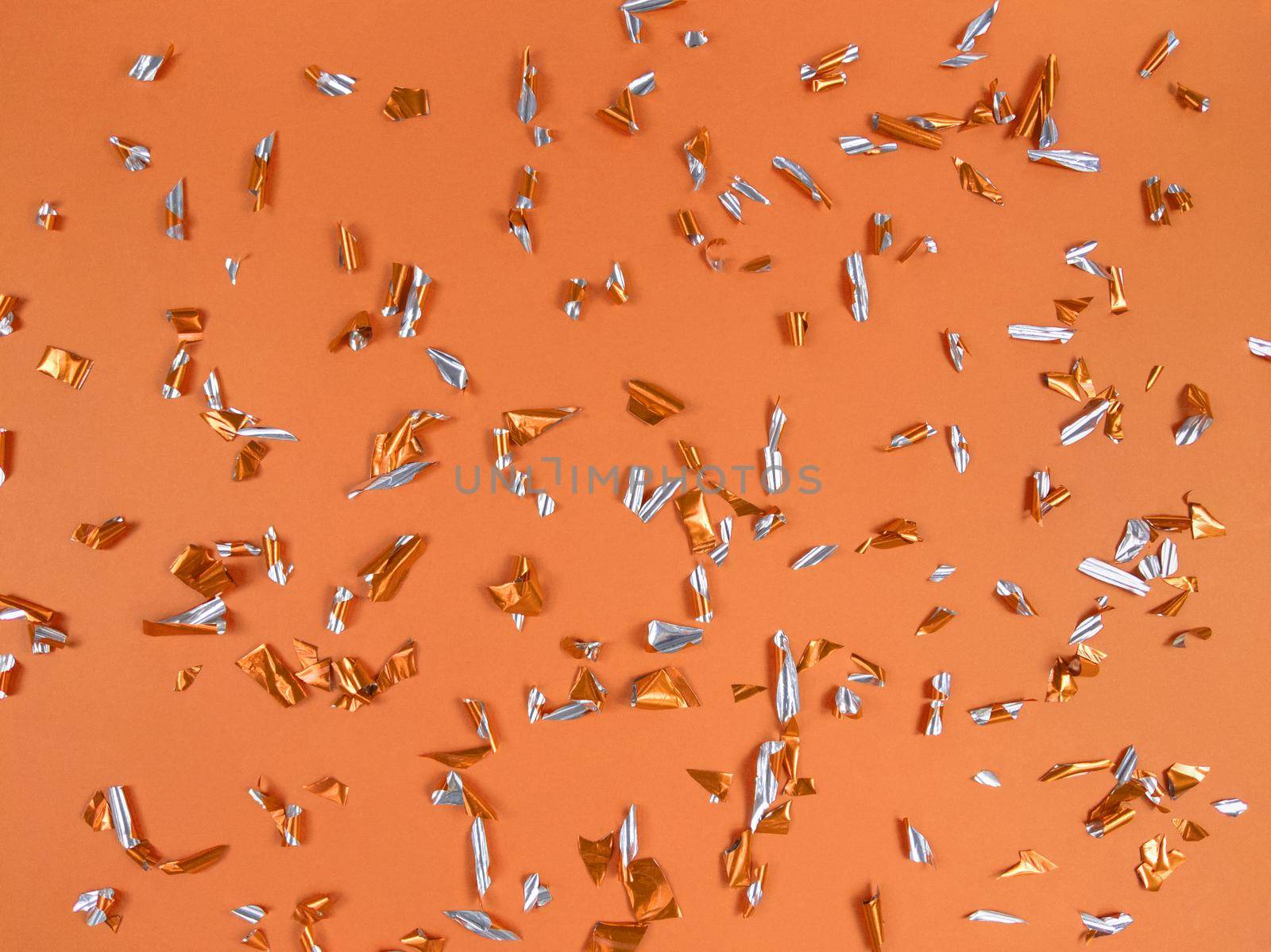 Confetti foil pieces on an orange background. Abstract festive backdrop.