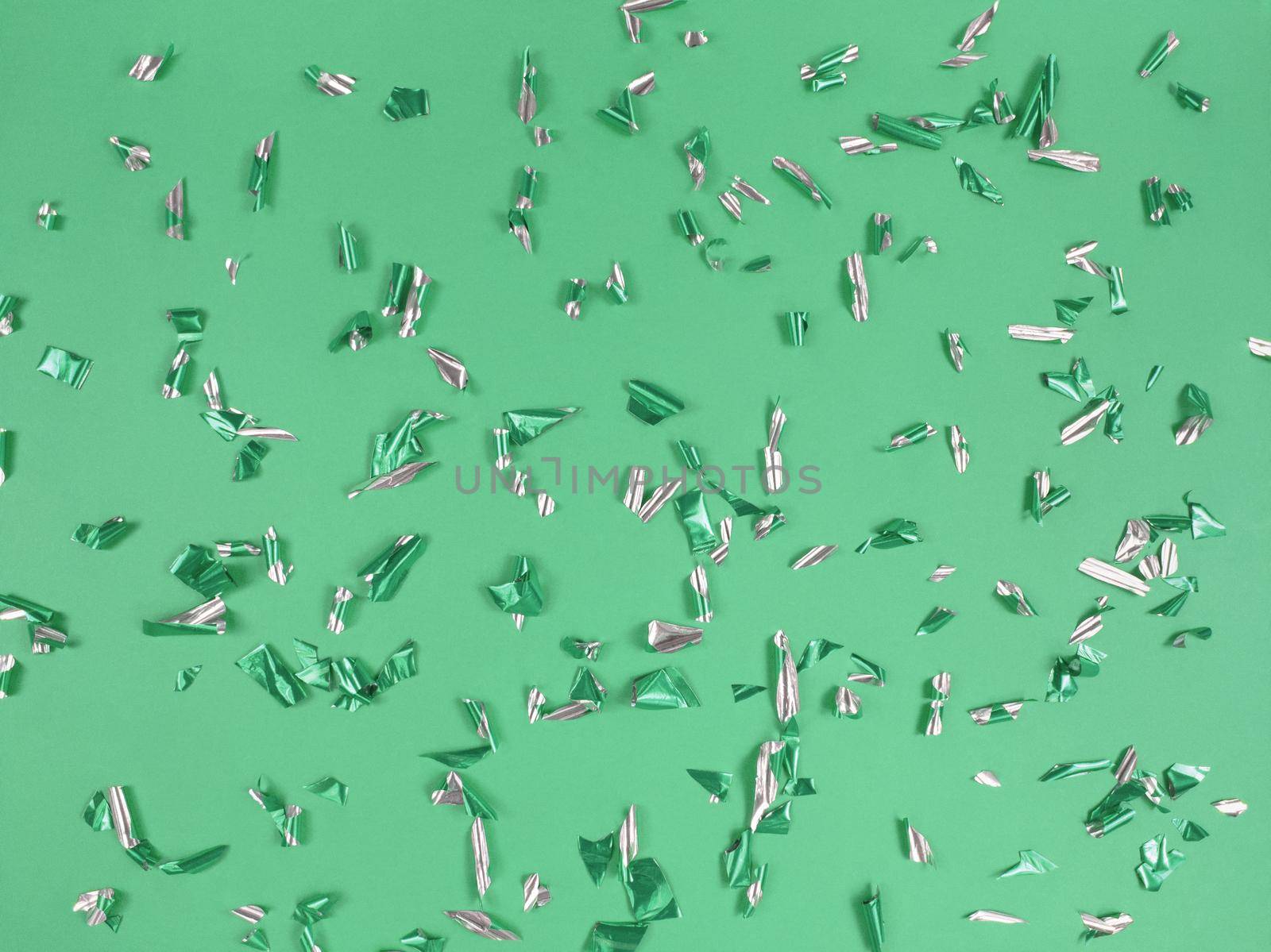 Confetti foil pieces on a green background. Abstract festive backdrop.