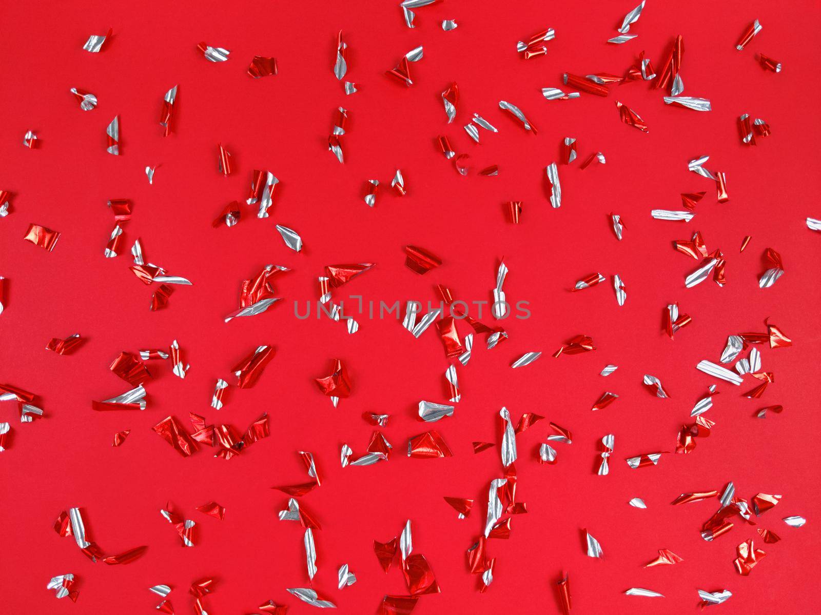 Confetti foil pieces on a red background. Abstract festive backdrop.