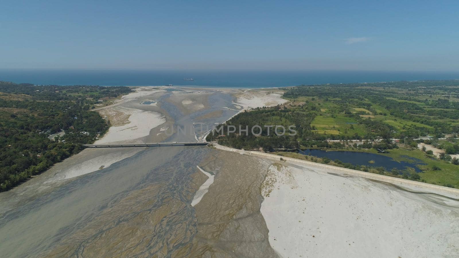 Mountain river Bucao flowing into the sea in Philippines,Luzon. Aerial view river among farmer fields flowing into the blue ocean.