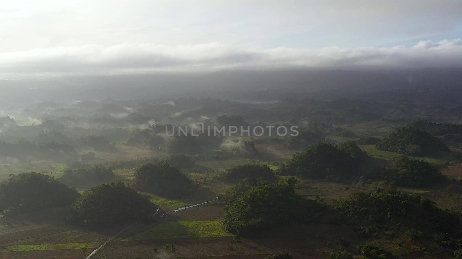 Tropical landscape with farmland and green hills, aerial view. The nature of Luzon Island, Philippines. Fog in the early morning.