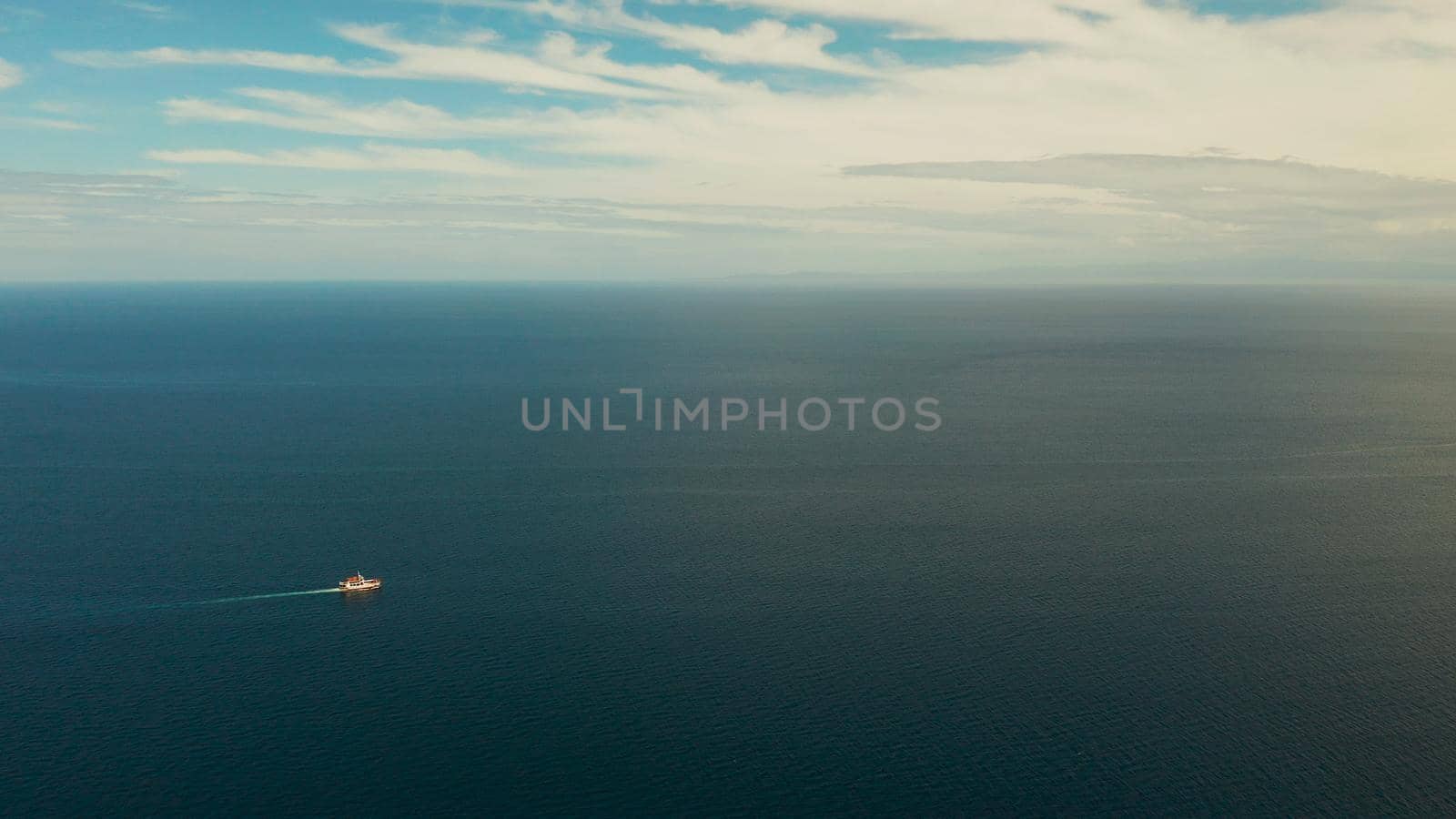 Small passenger ferry cruising in the open blue sea against blue sky with clouds, aerial view. Seascape: assenger ferry boat in open waters Philippines, Mindanao