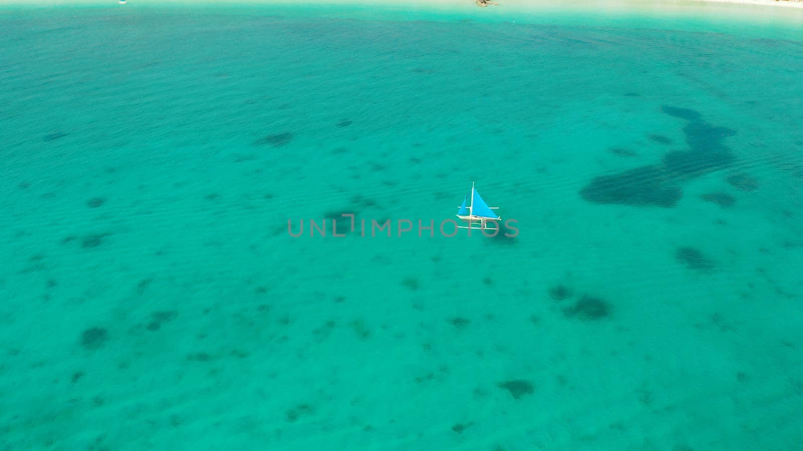 Sailing yacht in crystal clear turquoise water, aerial view. Sailing boat glides over the waves, Boracay, Philippines.