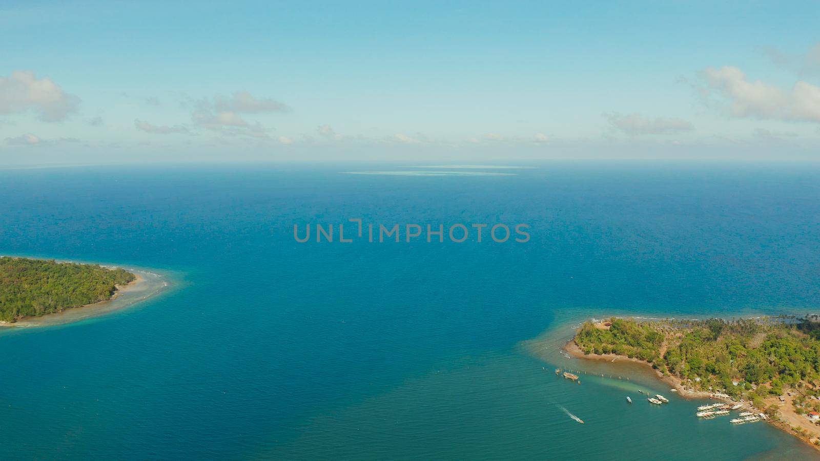 Seascape: shore of island Balabac with forest and palm trees, coral reef with turquoise water, top view. Coastline of tropical island covered with green forest against the blue sky with clouds and blue sea