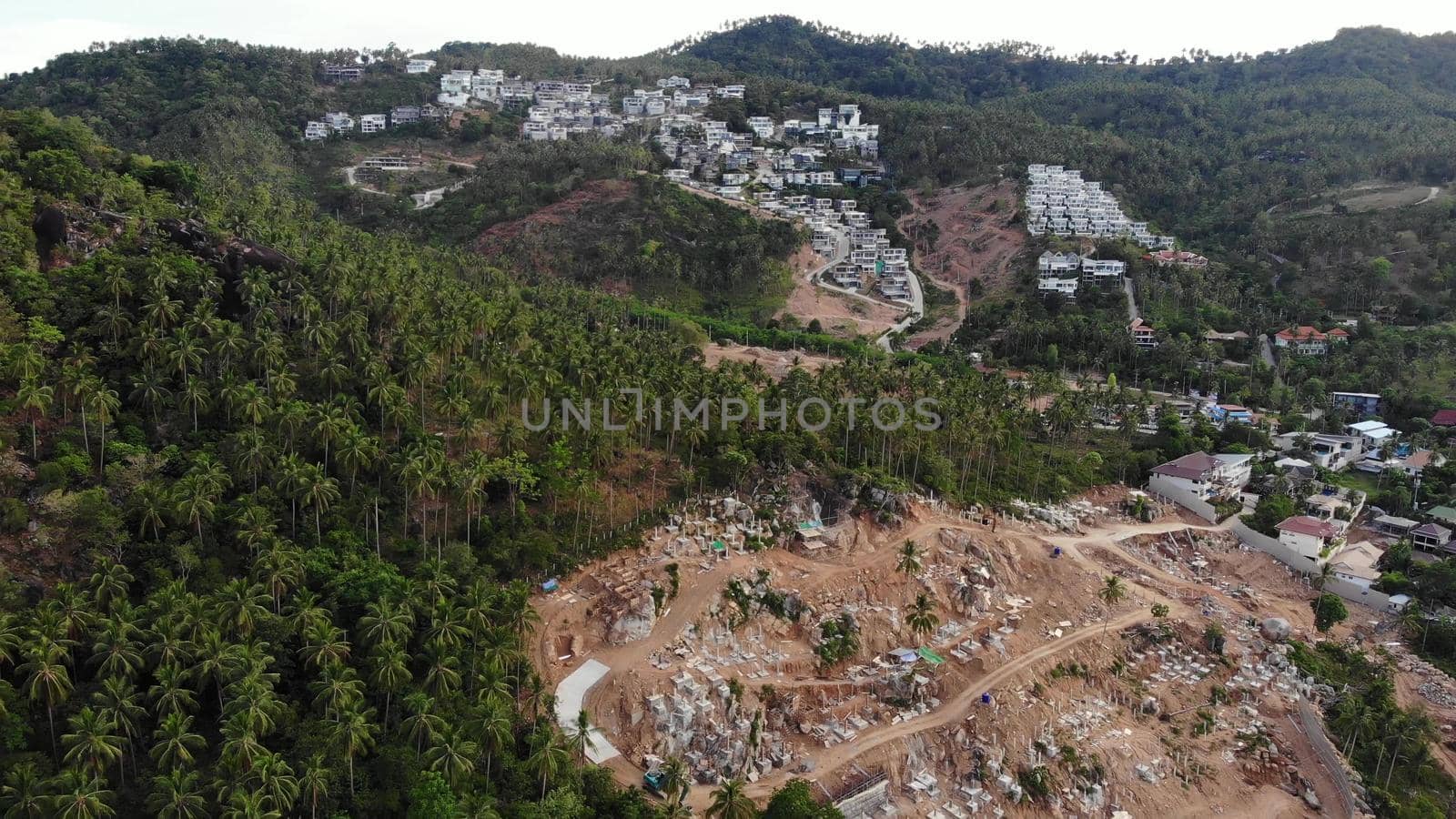 Tropical terrain covered with endangered forests and luxury villas. Drone view of large tropics with ecosystem disturbance due to buildings and deforestation. Koh Samui. Coconut palm plantations