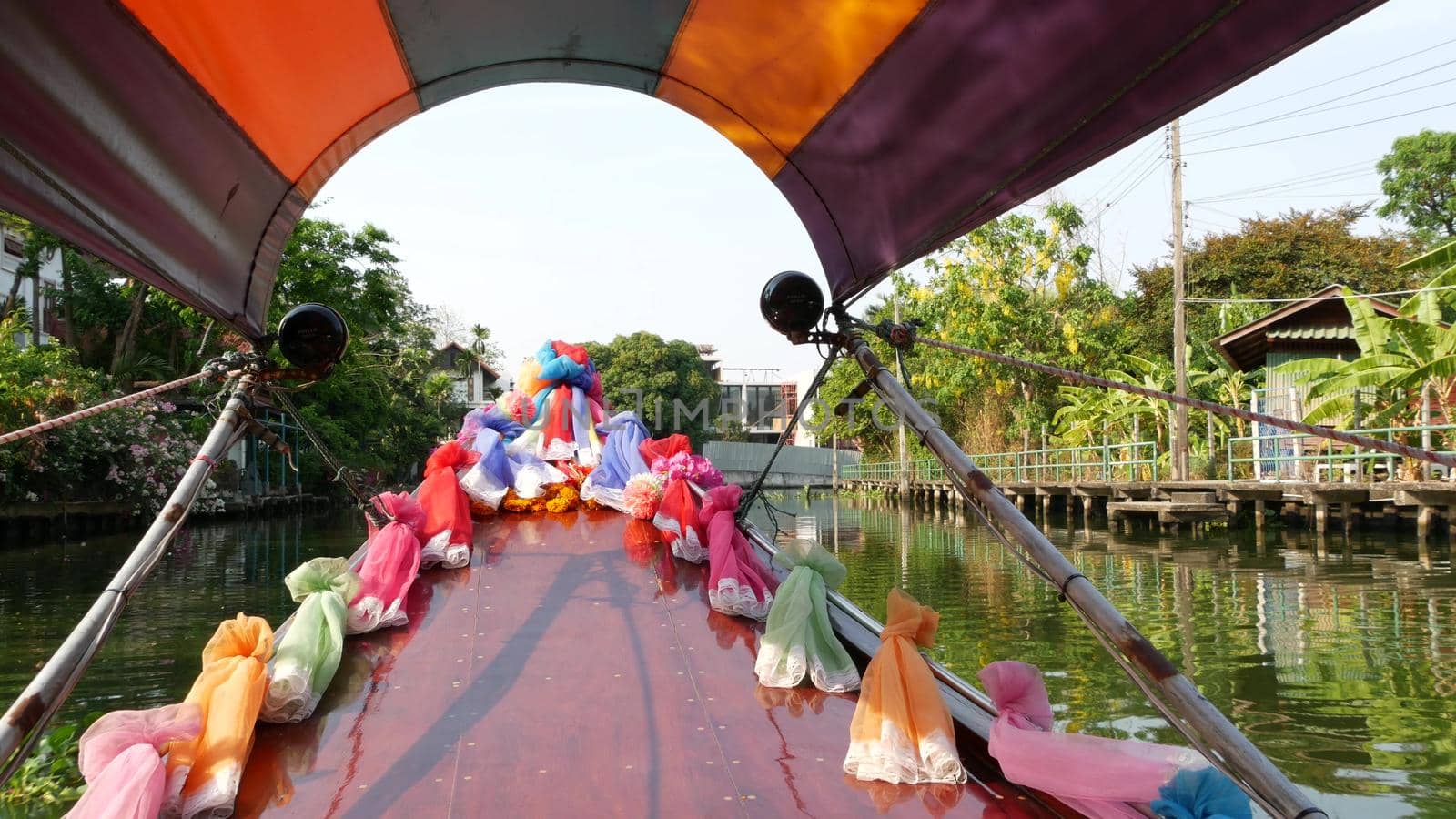 Tourist trip on Asian canal. View of calm channel and residential houses from decorated traditional Thai boat during tourist trip in Bangkok