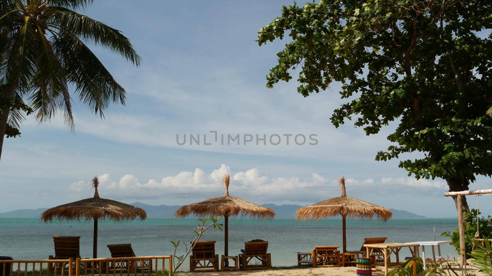 Sunshades on sea background. Sun umbrellas from straw and palm trees on ocean and sky background in Thailand. Relax, Travel vacation holiday resort concept