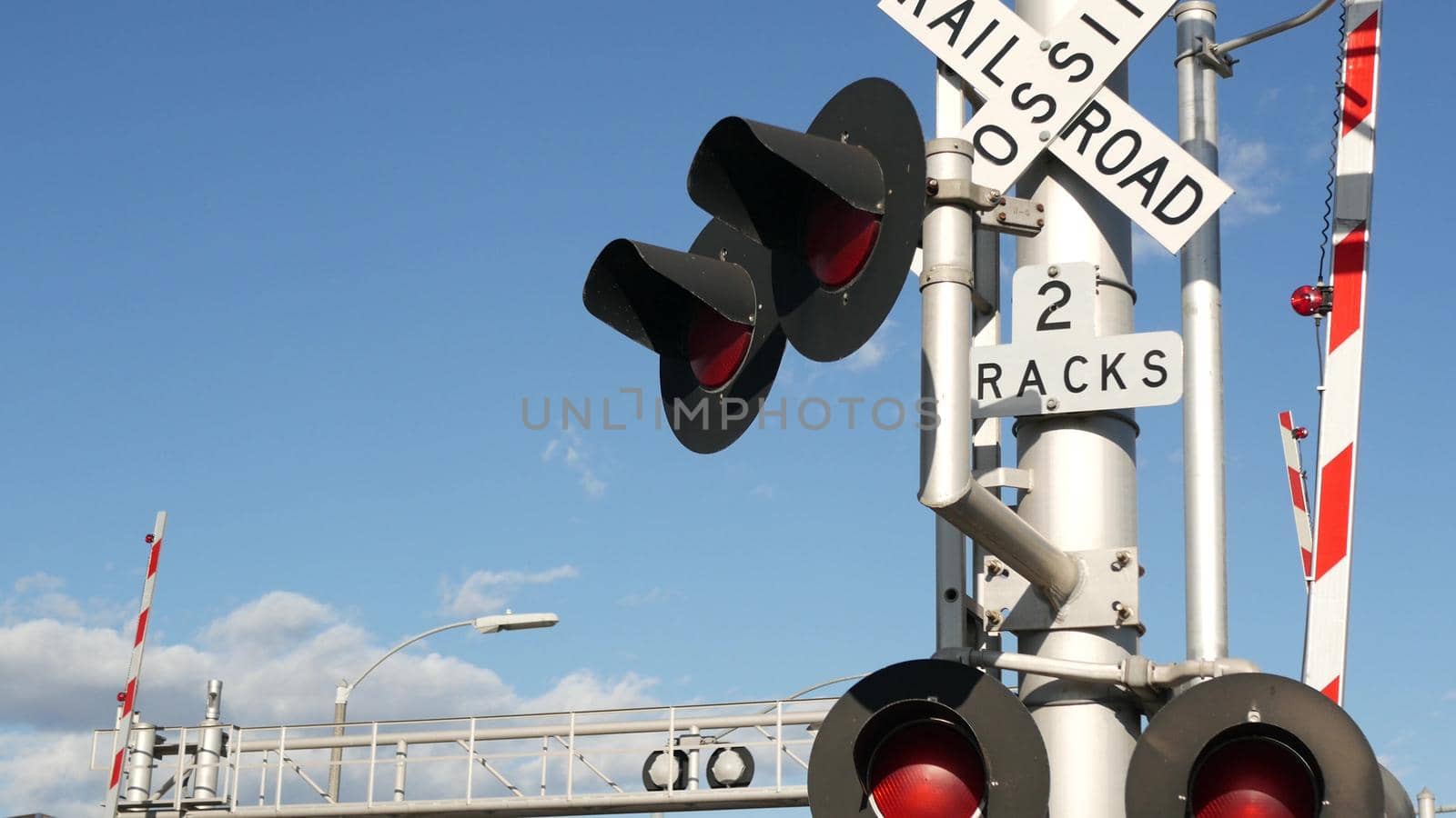 Level crossing warning signal in USA. Crossbuck notice and red traffic light on rail road intersection in California. Railway transportation safety symbol. Caution sign about hazard and train track.