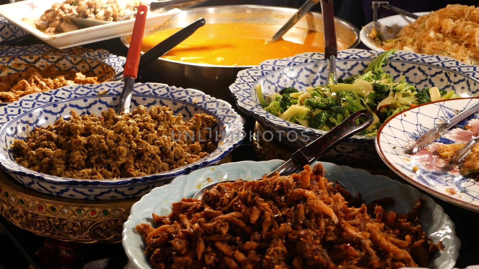 Bowls with various Asian dishes on stall. Bowls of assorted traditional Thai dishes placed on stall of street diner in evening. Oriental night market food court