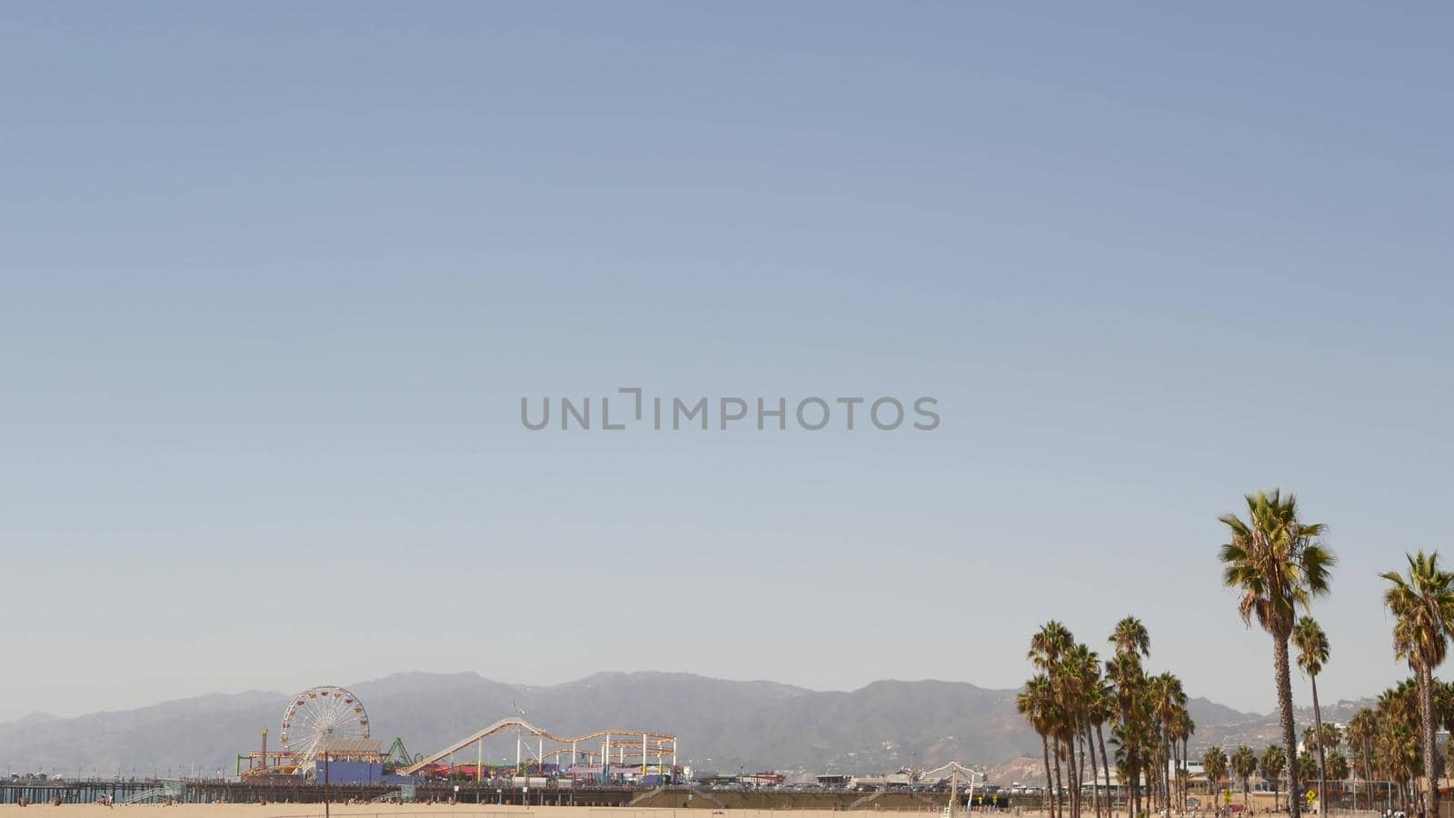 California beach aesthetic, classic ferris wheel, amusement park on pier in Santa Monica pacific ocean resort. Summertime iconic view, palm trees and sky, symbol of Los Angeles with copy space, CA USA by DogoraSun