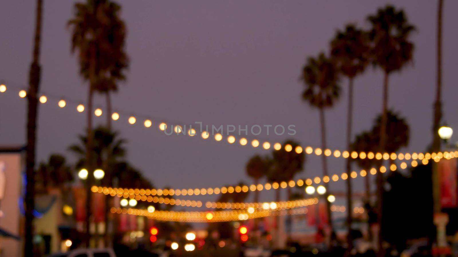 Decorative staring garland lights, palm trees silhouettes, evening sky. Blurred Background. Street decorated with lamps in California. Festive illuminations, beach party, tropical vacations concept