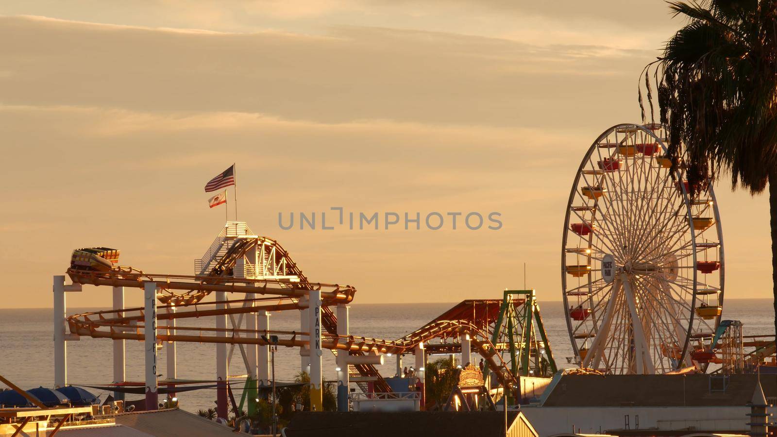 Classic ferris wheel, amusement park on pier in Santa Monica pacific ocean beach resort. Summertime California aesthetic, iconic view, symbol of Los Angeles, CA USA. Sunset golden sky and attractions.