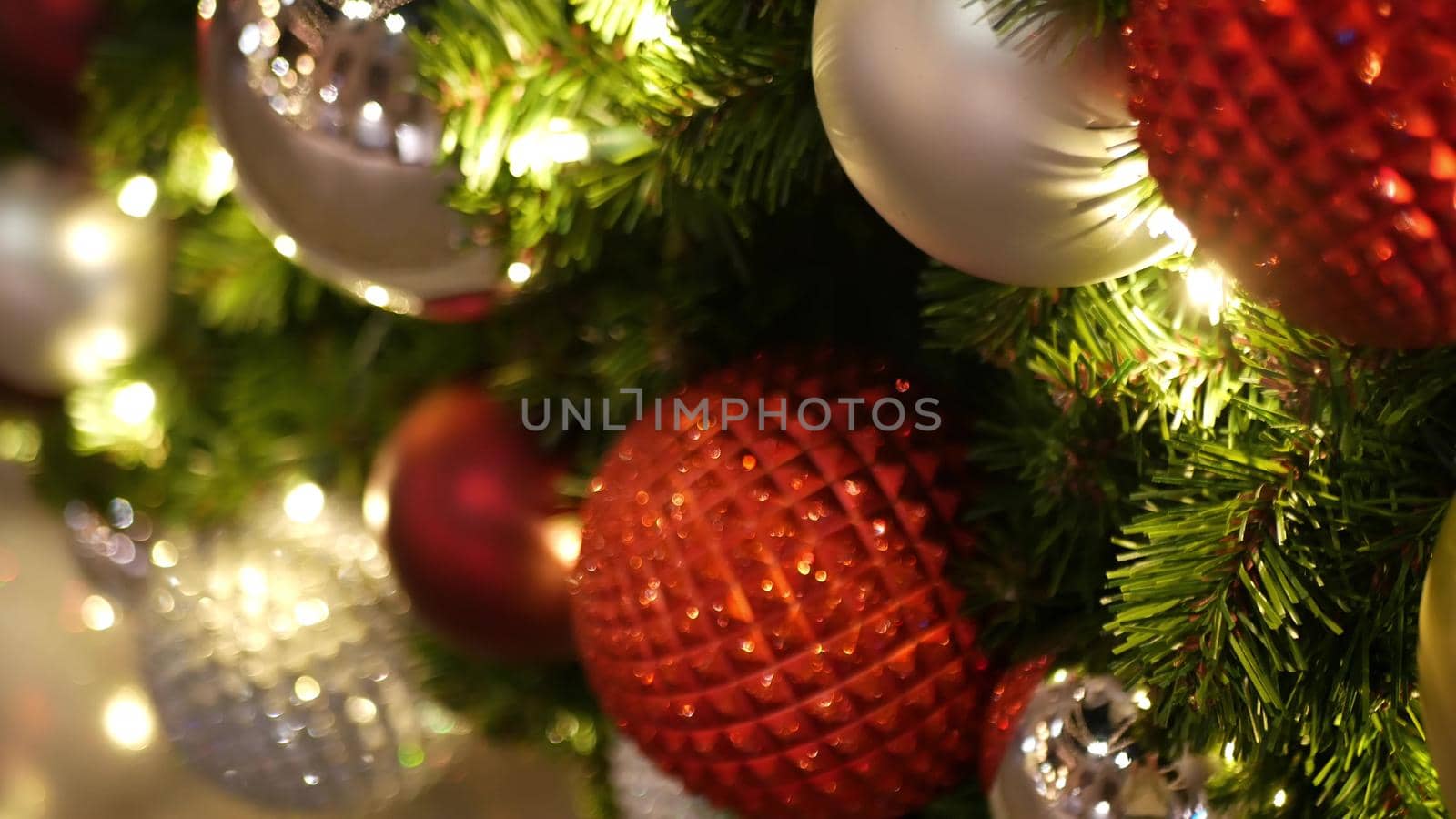 Closeup of Festively Decorated Outdoor Christmas tree with bright red balls on blurred sparkling fairy background. Defocused garland lights, Bokeh effect. Merry Christmas and Happy Holidays concept. by DogoraSun