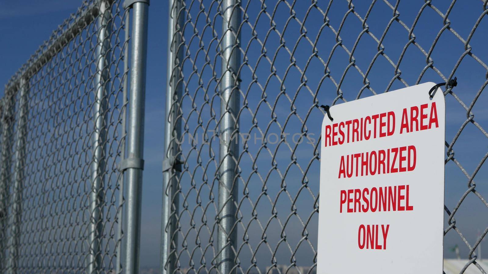 Restricted area, authorized personnel only sign in USA. Red letters, keep off warning on metal fence, United States border symbol. No trespassing notice means violators will be prosecuted by US law by DogoraSun