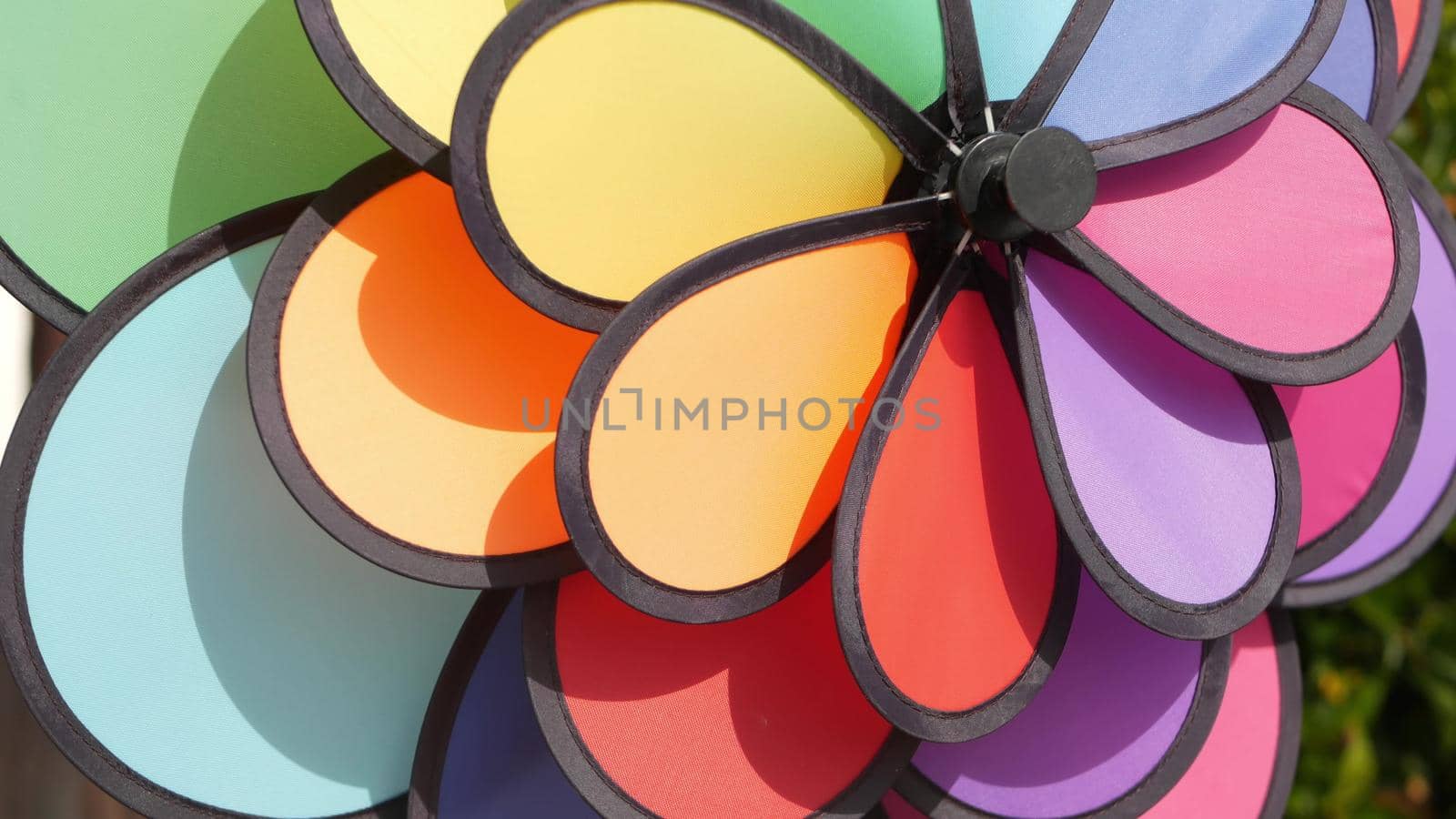 Colorful pinwheel spinning, weather wind vane, garden decoration in USA. Rainbow symbol of childhood, fantasy and imagination rotating. Multi colored spiral toy turning in breeze. Summertime dreaming.