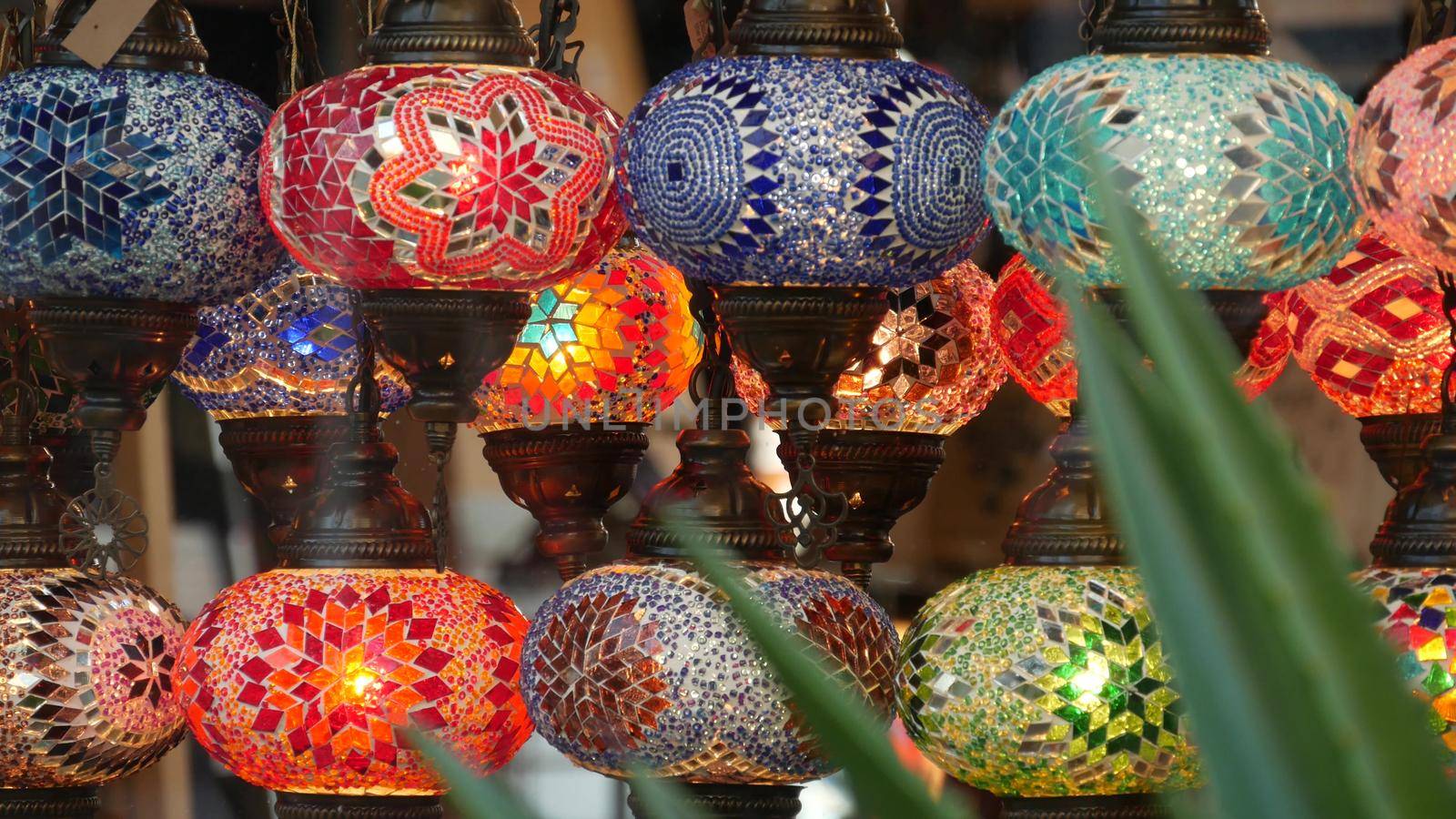 Colourful turkish lamps from glass mosaic glowing. Arabic multi colored authentic retro style lights. Many illuminated moroccan craft lanterns. Oriental islamic middle eastern decor. Shiny folk shop.