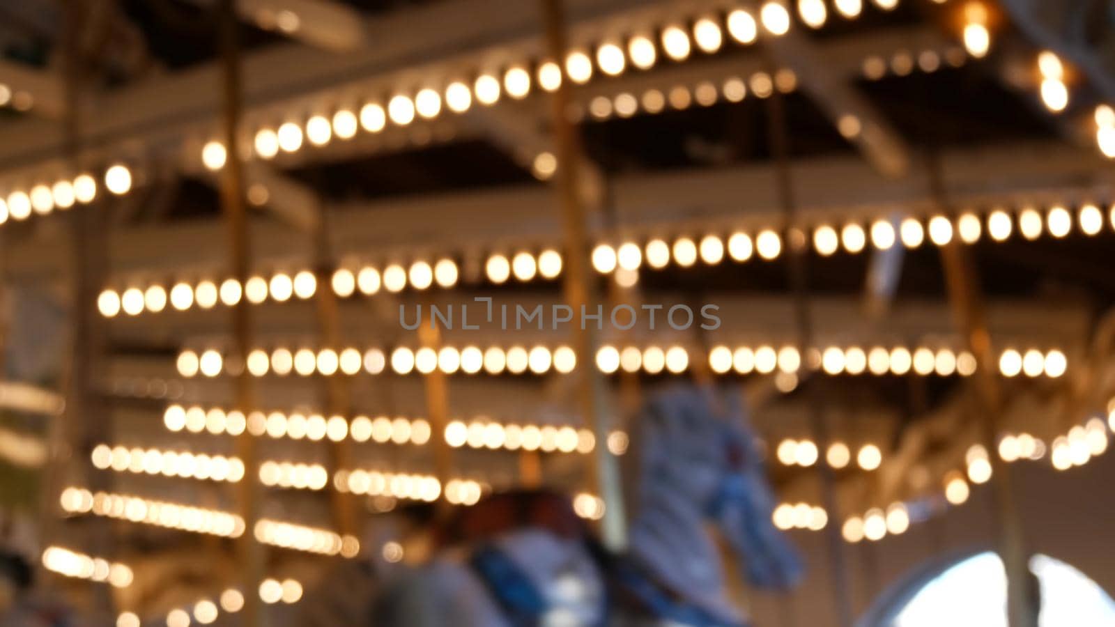 Golden illuminated defocused retro carousel turning in amusement park. Blurred shiny merry-go-round glowing and rotating at night. Radiant spinning symbol of childhood. Festival atmosphere of funfair.