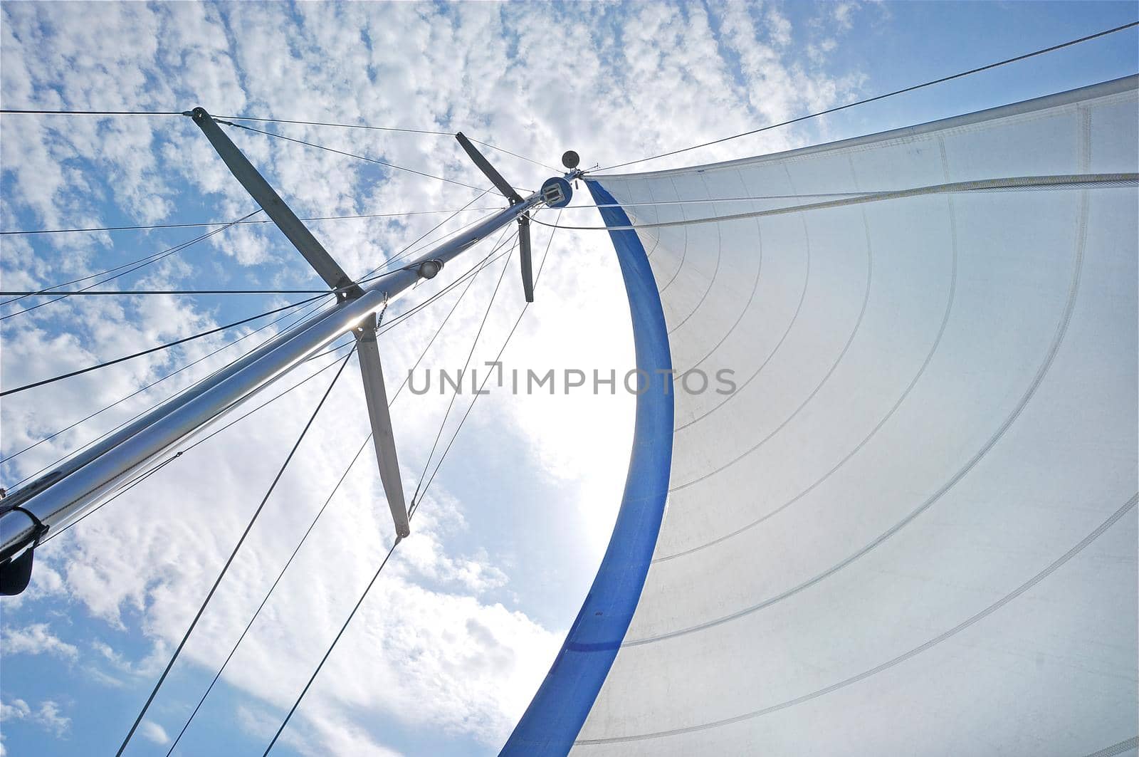 From below shot of white waving sail on tall mast under blue sky in clouds . White sail on mast under blue sky