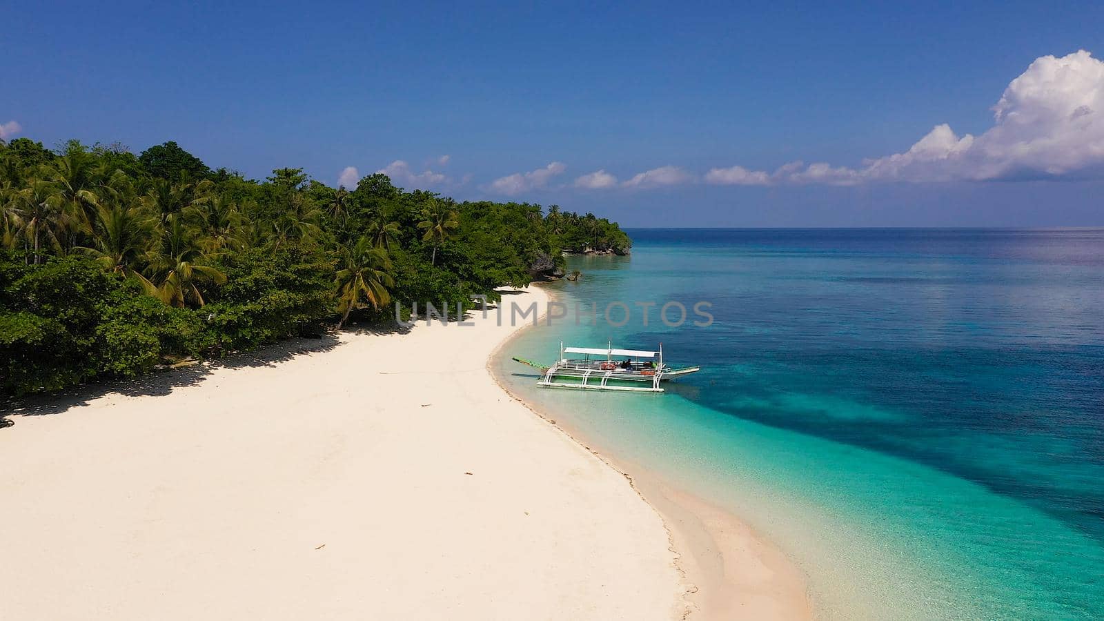 Tropical beach of white sand, top view. Tranquil beach scene. Tourist boat off the coast. Blue sea with turquoise lagoons. Coral reef near the beach. Summer and travel vacation concept.