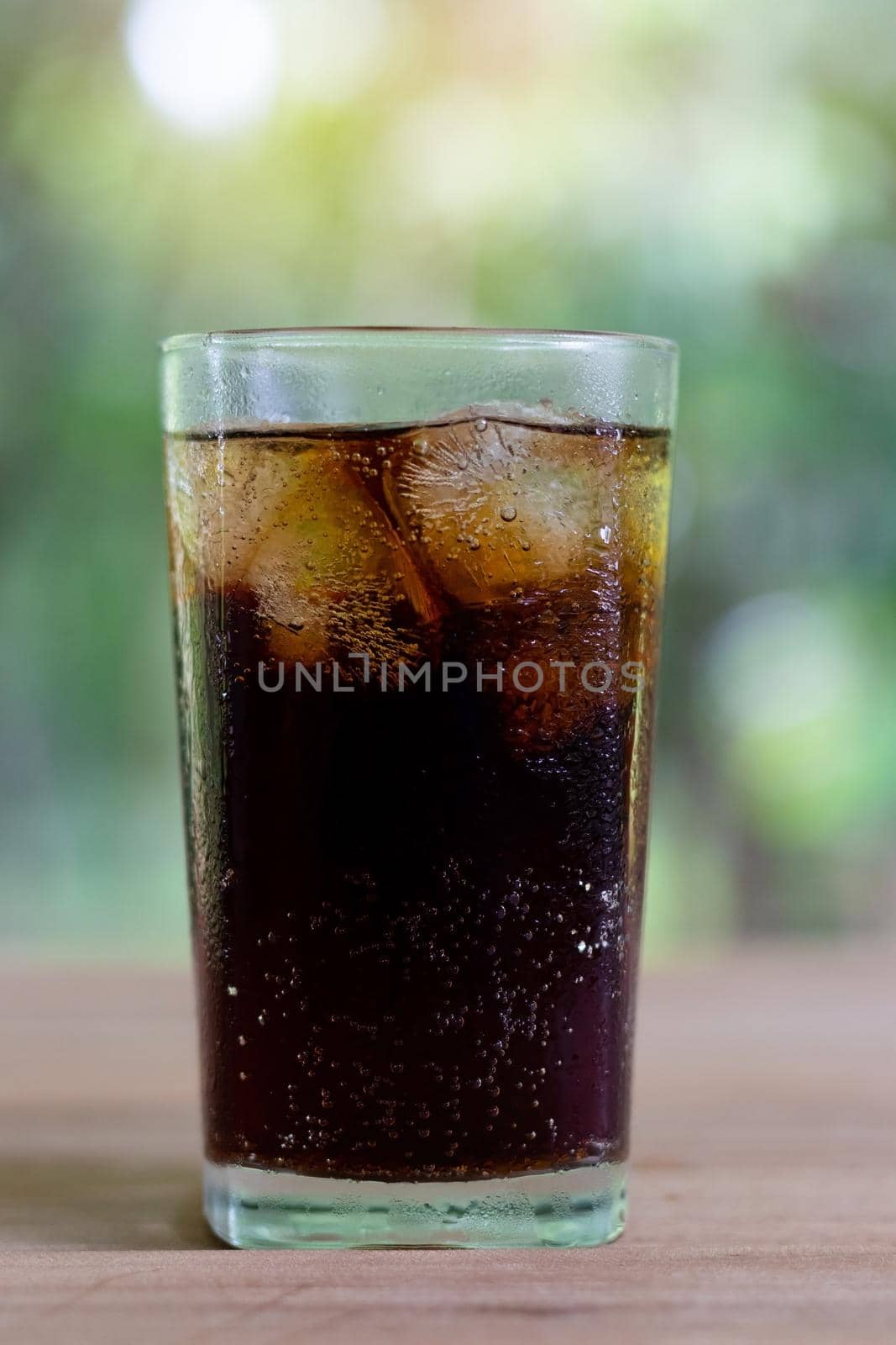 Refreshing black soda soft drinks or cola with ice in a clear tall glass with nature background.