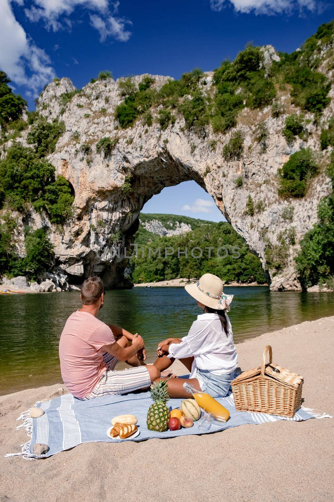 couple men and woman picnic on the beach of the The famous natural bridge of Pont d'Arc in Ardeche department in France Ardeche. Europe Rhone Alpes