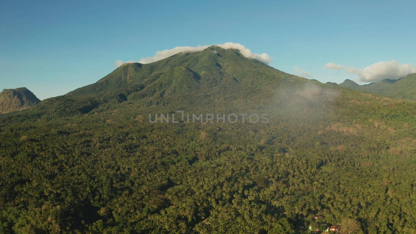 Mountains covered rainforest, trees and blue sky with clouds, aerial view. Camiguin, Philippines. Mountain landscape on tropical island with mountain peaks covered with forest. Slopes of mountains with evergreen vegetation.