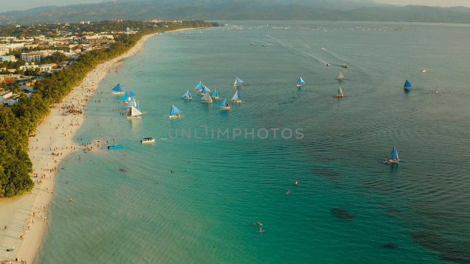 Topical white beach from above at sunset with tourists and sailing yachts on Boracay Island. Tropical white beach with sailing boat. Summer and travel vacation concept.