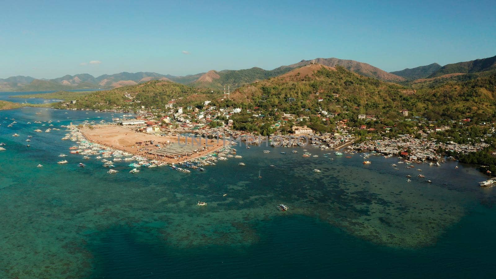 aerial view City Quay with boat dock and public market Coron town, tourist destination in the Philippines. Pier and promenade with boats on Busuanga island. Wooden boats waiting at pier. Seascape with mountains.