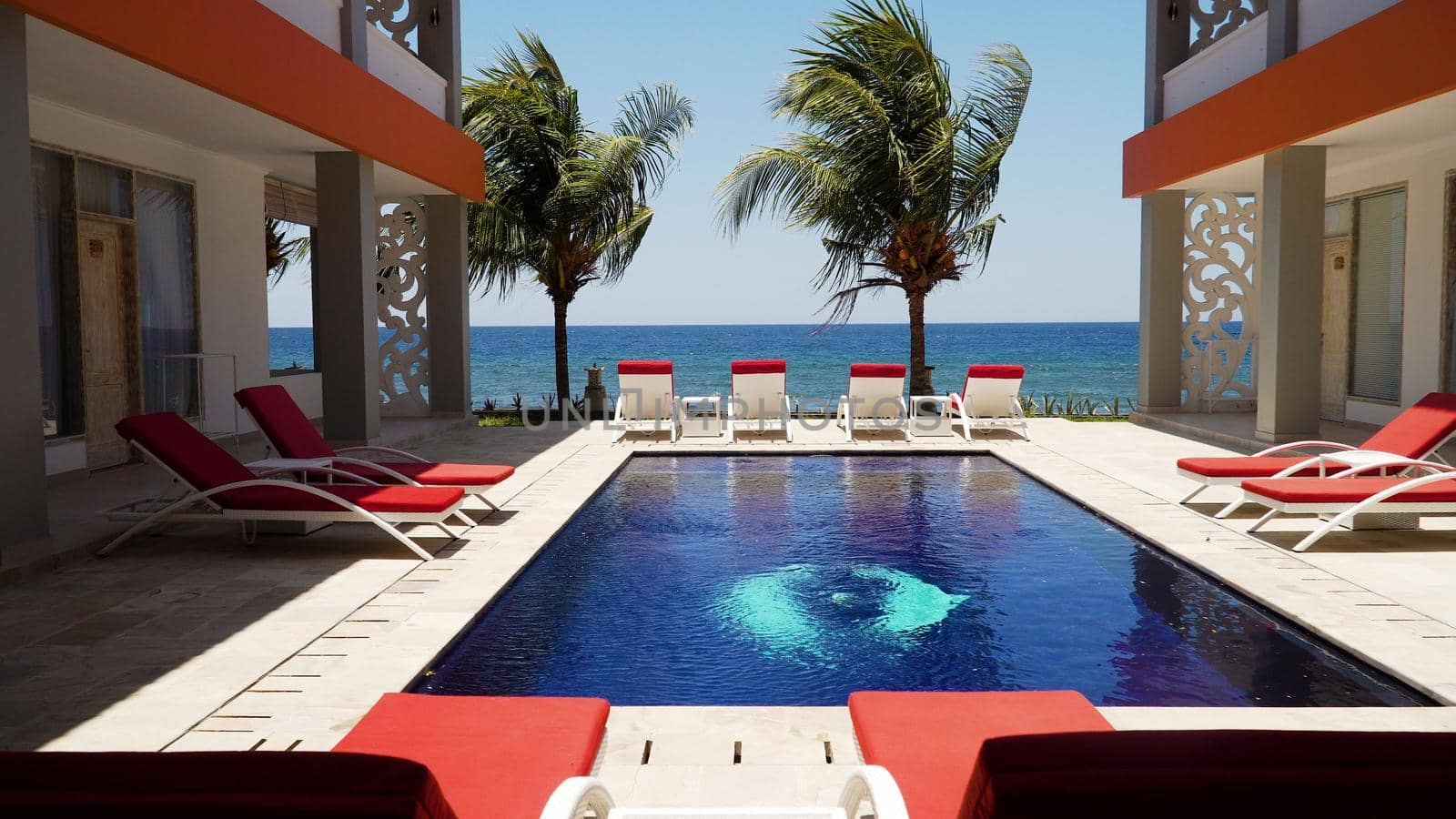 luxury hotel with swimming pool, sun beds, palm trees by sea. tropical resort with pool. Travel concept.