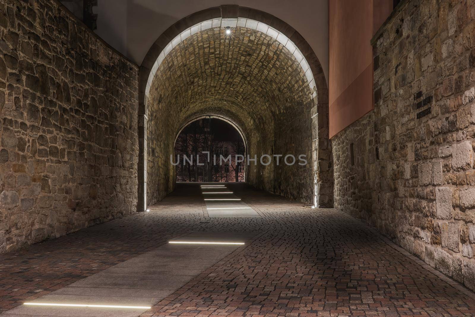 An old illuminated historic tunnel in the old town and old stones on the walls by silent303