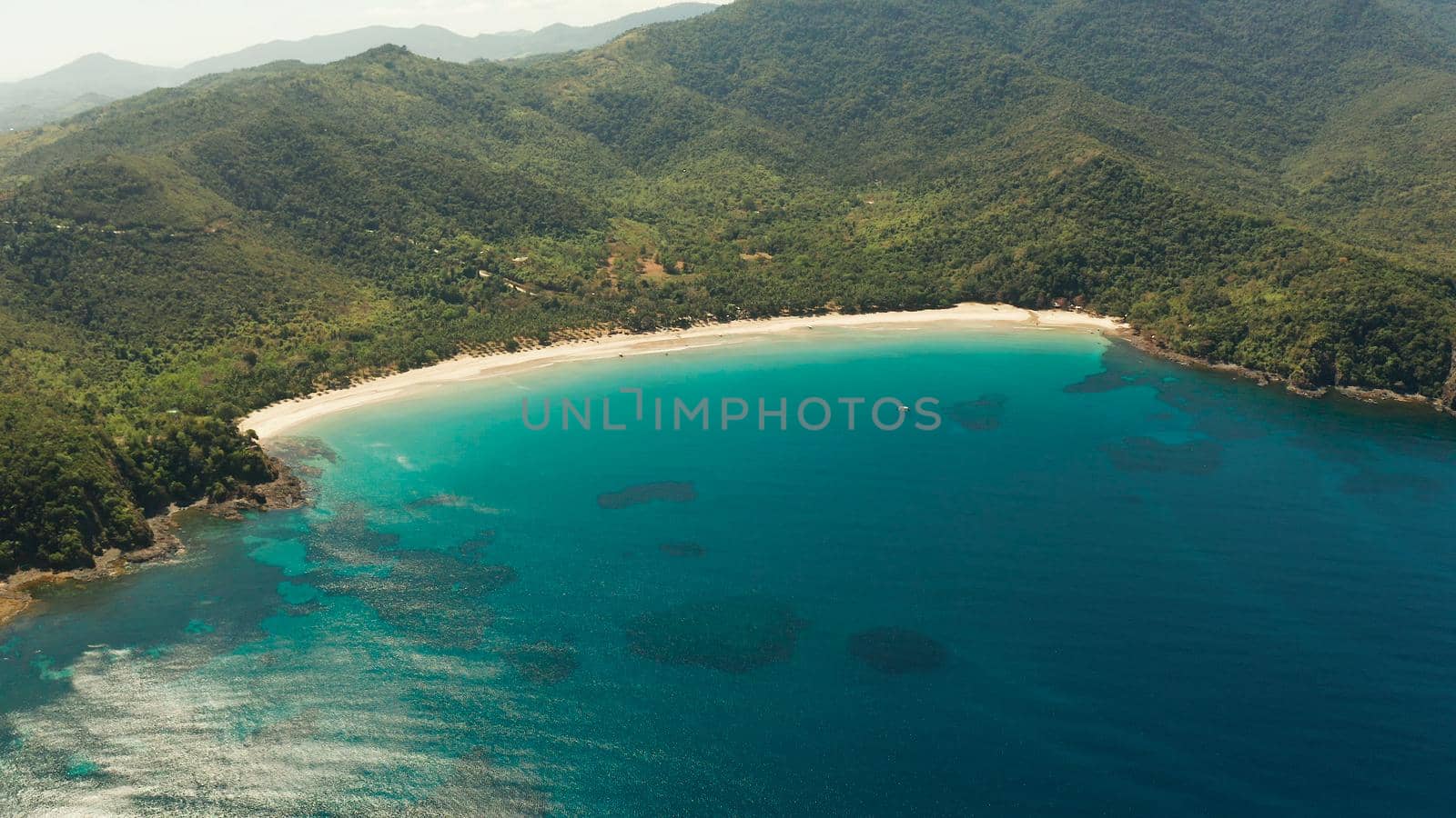 Aerial view beautiful tropical beach Nagtabon in the cove with blue lagoon and turquoise water surrounded by rainforest. Palawan, Philippines. tropical landscape. Seascape island and clear blue water. Summer and travel vacation concept