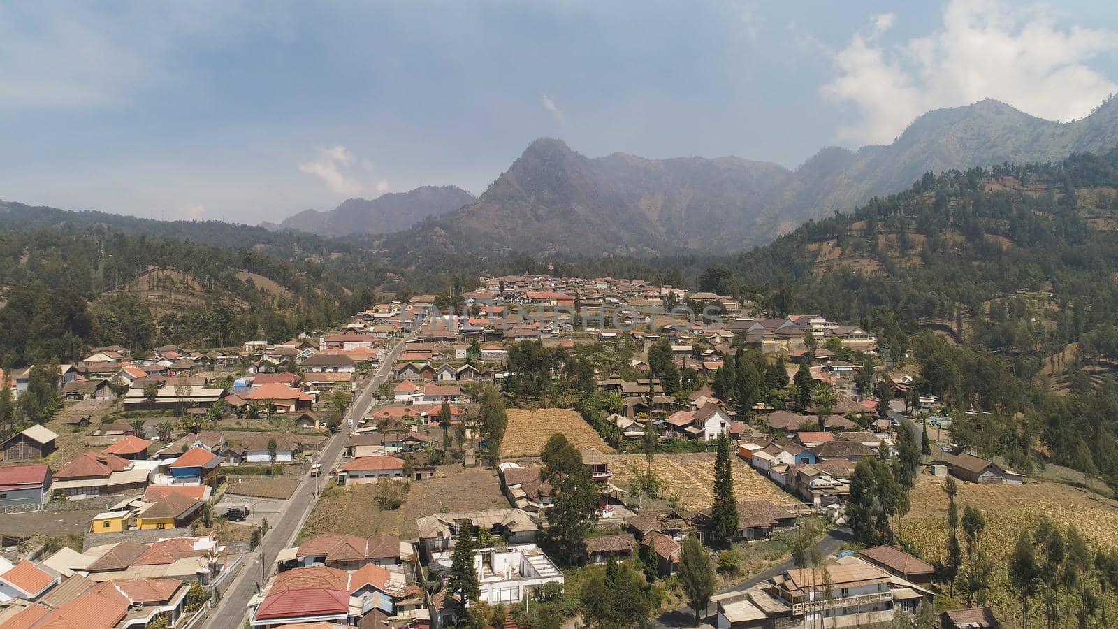 village in mountain valley. mountains with farmlands, village, fields with crops, trees. Aerial view farm lands on mountainside. tropical landscape Java Indonesia.
