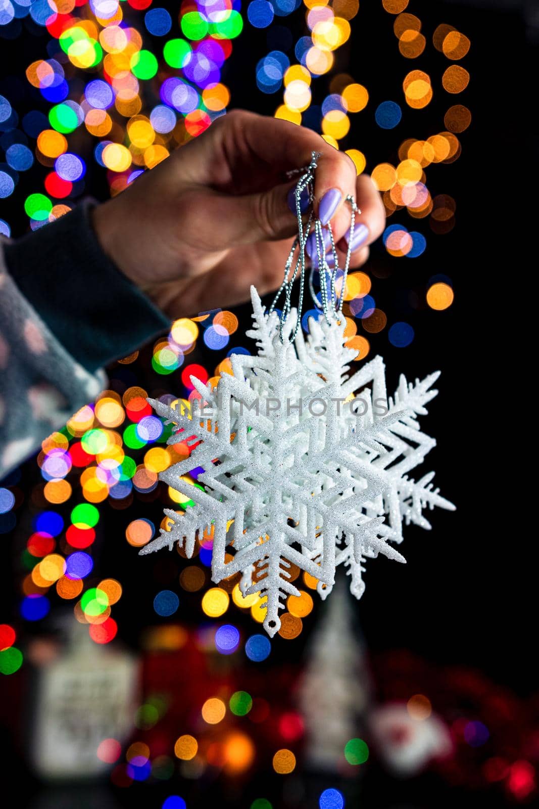 Holding Christmas snowflake decoration isolated on background with blurred lights. December season, Christmas composition. by vladispas