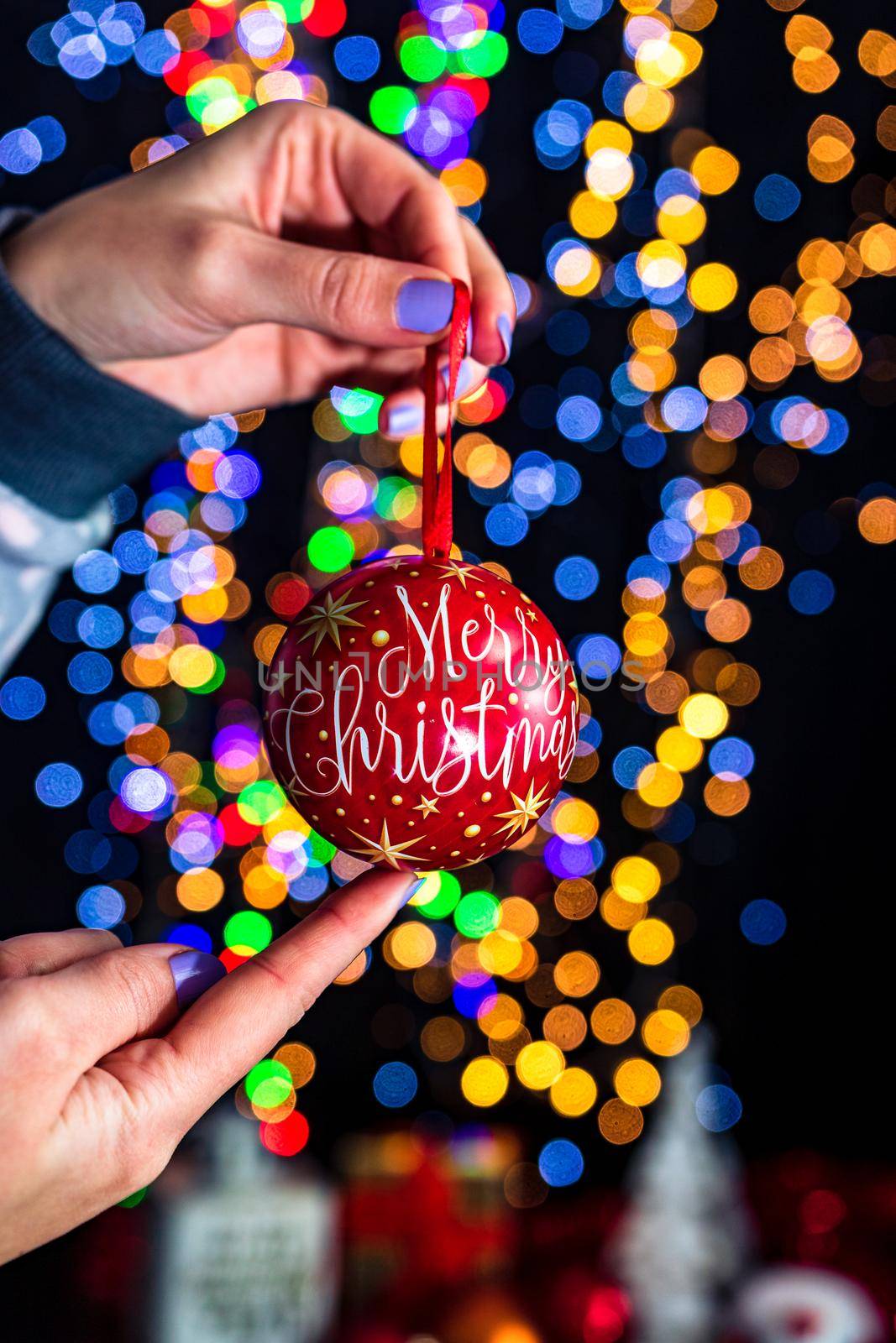 Holding Merry Christmas bauble decoration isolated on background with blurred lights. December season, Christmas composition.
