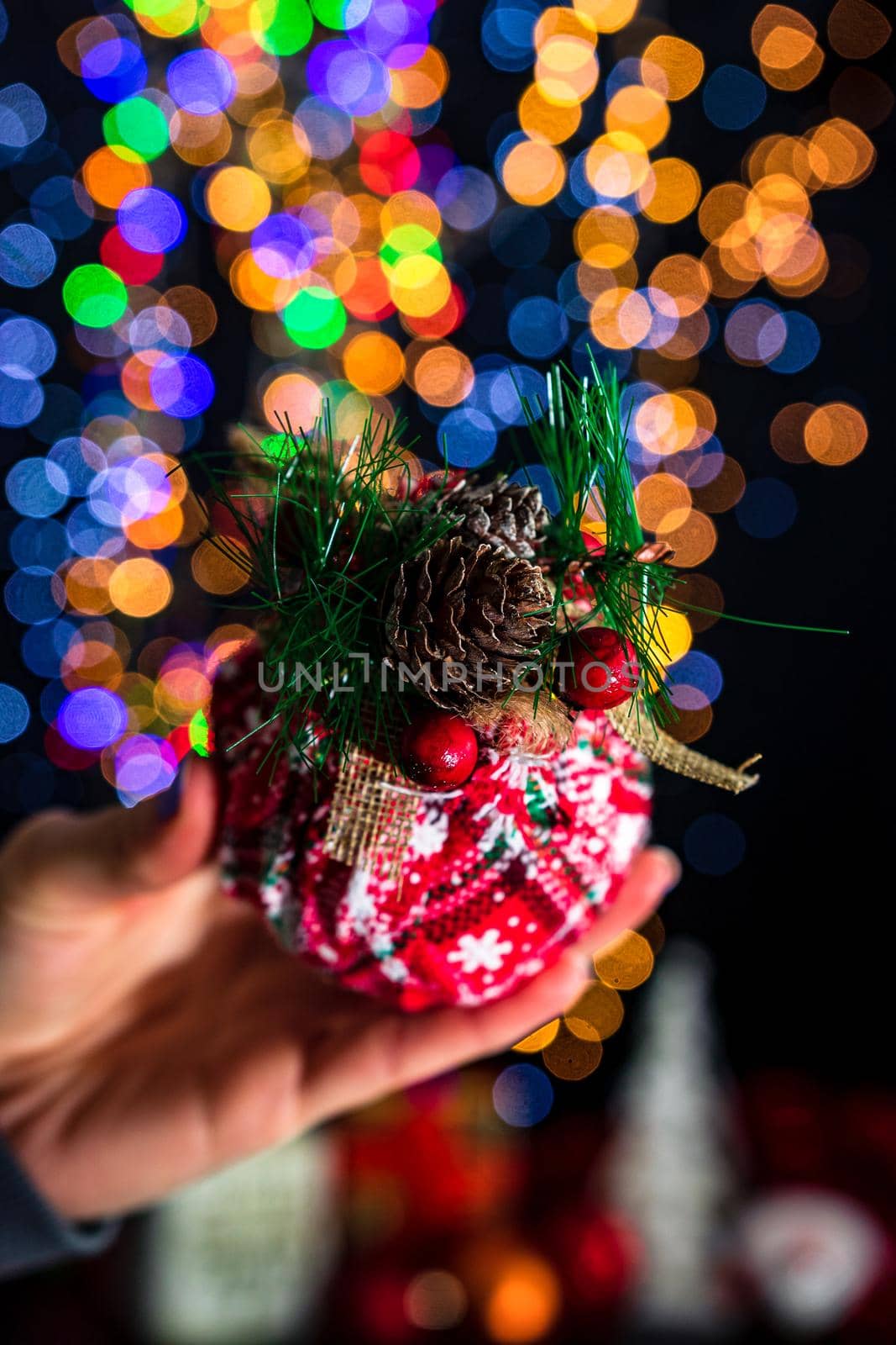 Holding Christmas bauble decoration isolated on background with blurred lights. December season, Christmas composition. by vladispas